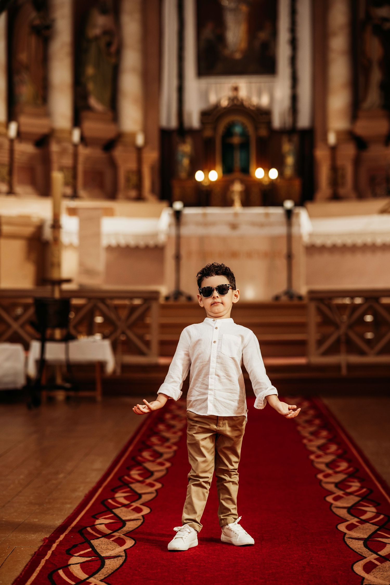 A young person in sunglasses and white shirt stands confidently on a red carpet inside an ornate church.