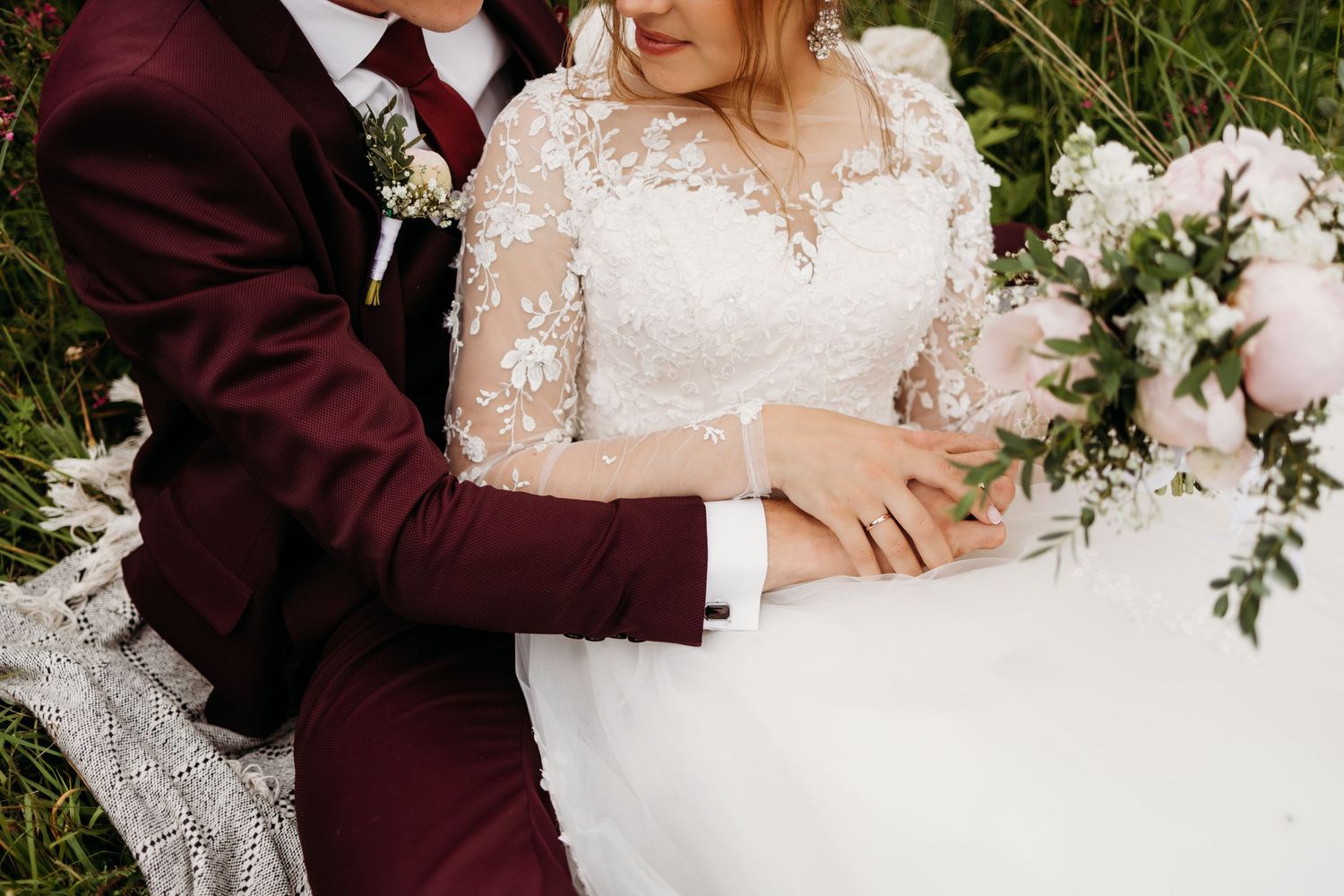 Wedding details showing burgundy suit and white lace dress with floral bouquet.