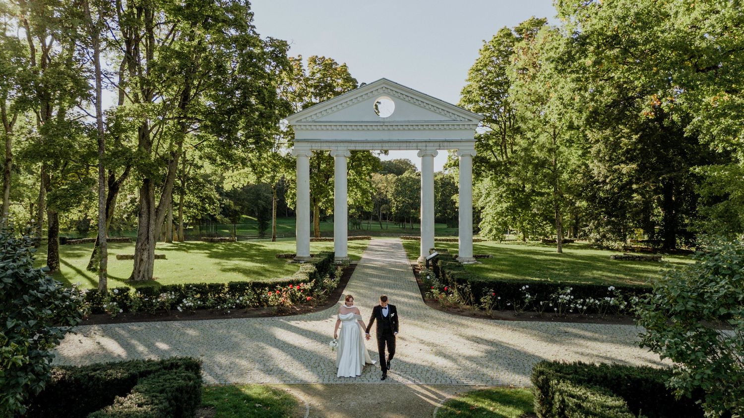 Panoramic view of a classic white columned wedding venue surrounded by lush green gardens.