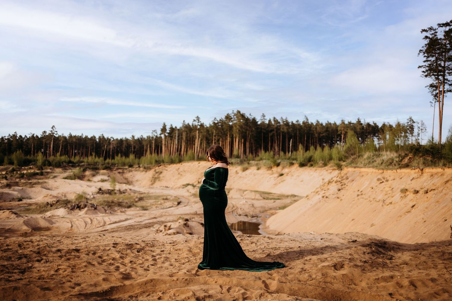 Silhouetted figure in dark clothing against sandy dunes and pine trees.