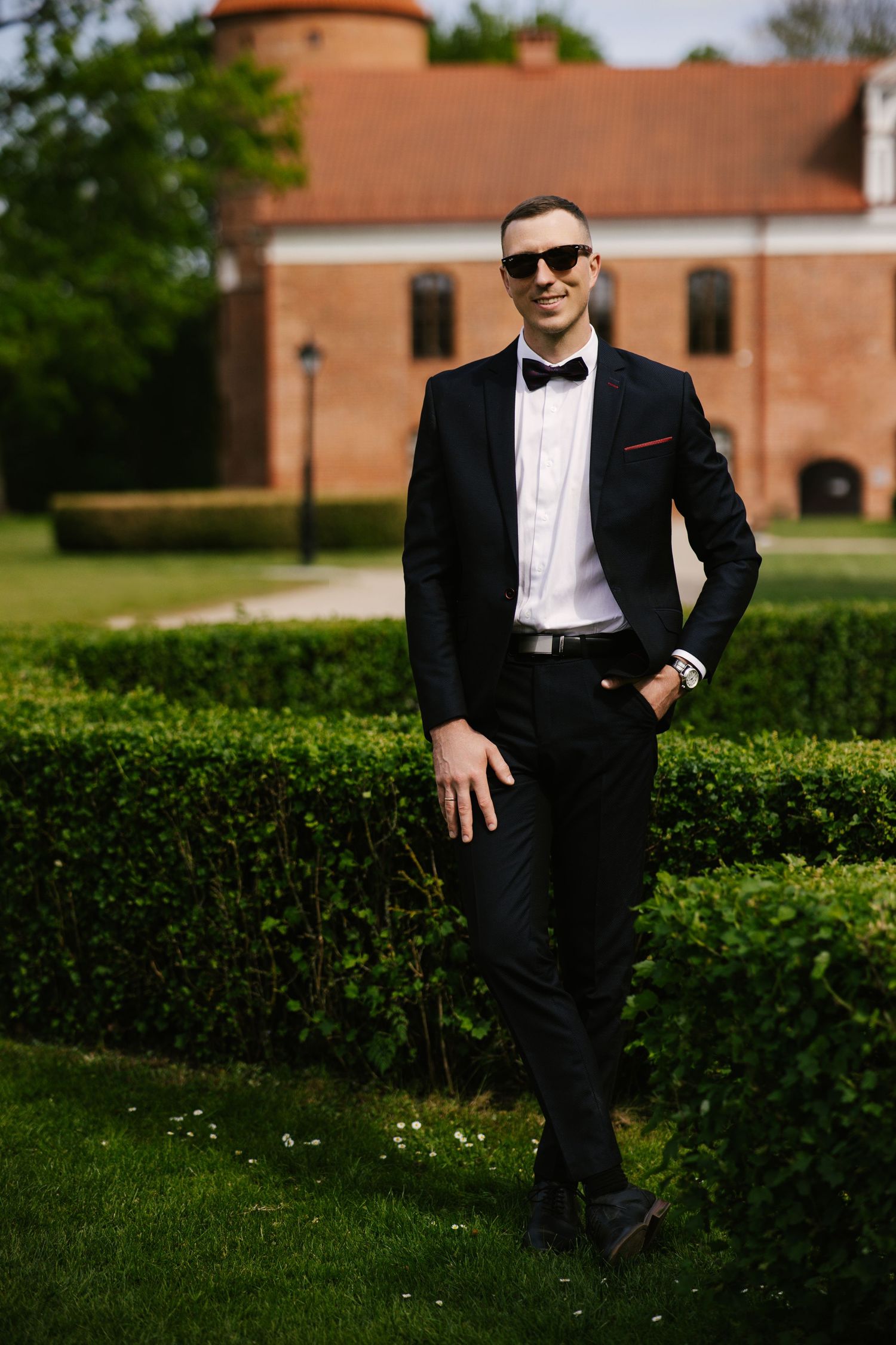 A formal portrait in front of a historic brick building showcasing classic black tie attire.