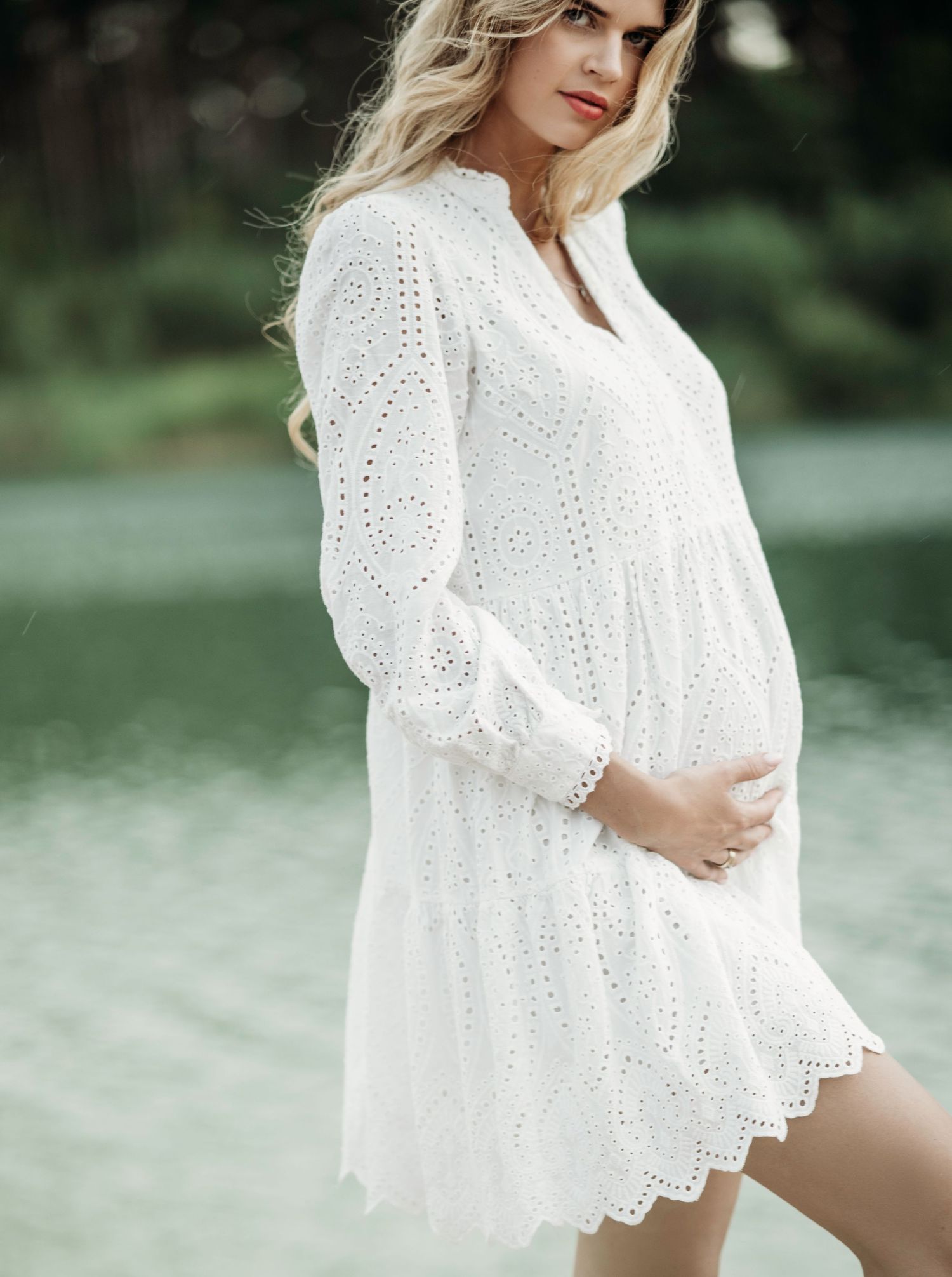Intimate maternity portraits in white lace dress near water.
