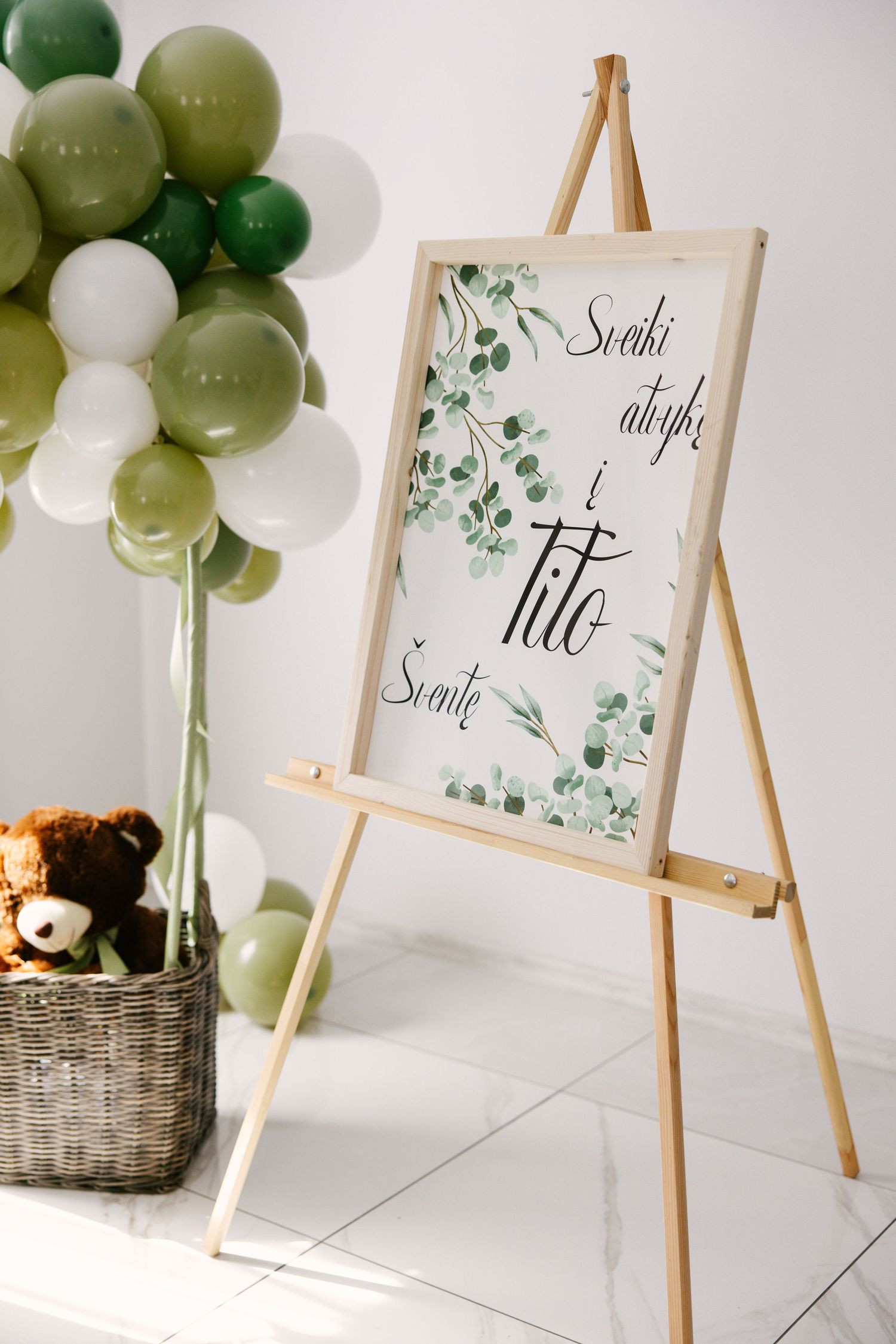 Green and white balloon arch with wooden easels displaying botanical signage.