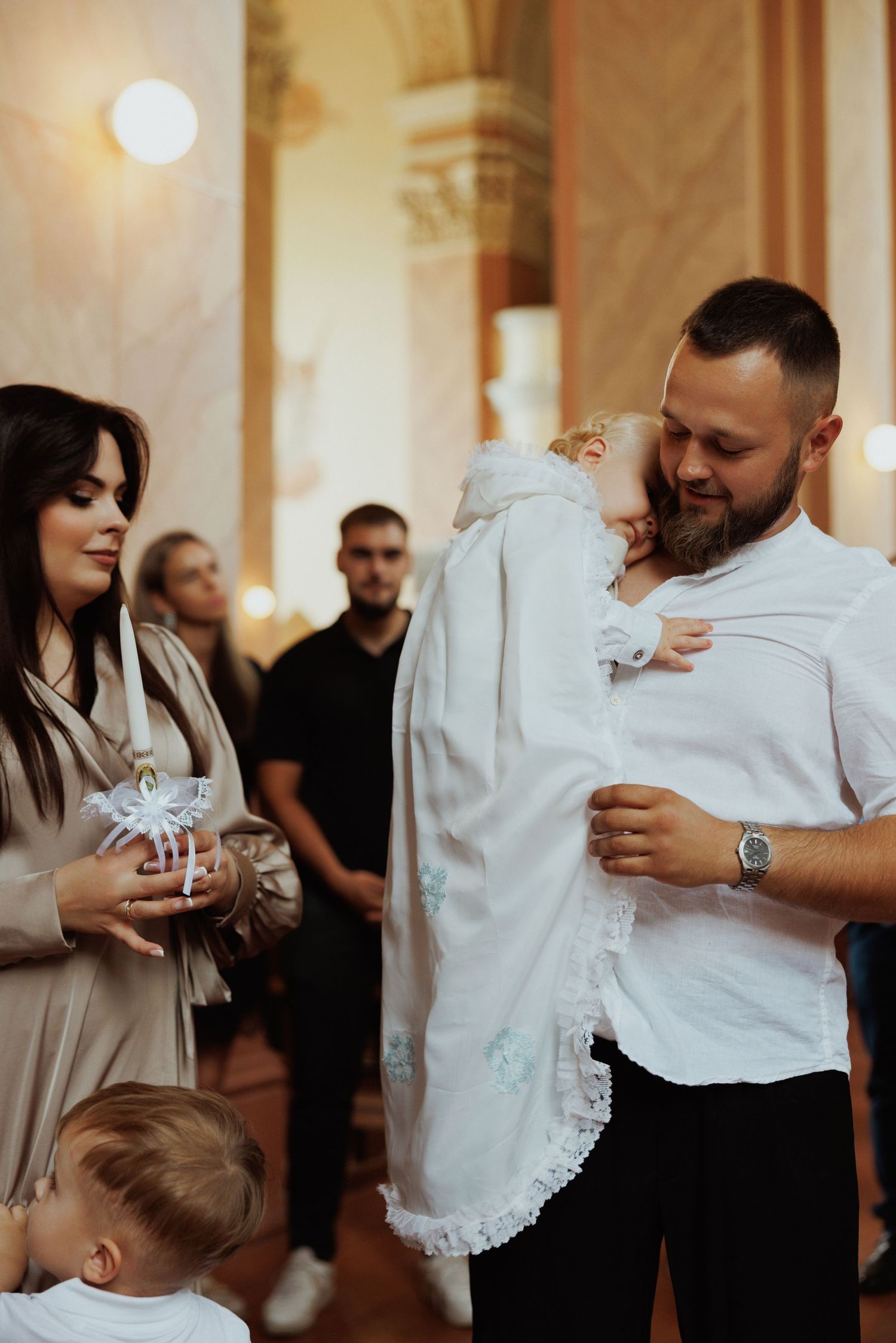 Baptism ceremony in church with white christening gown and family members.