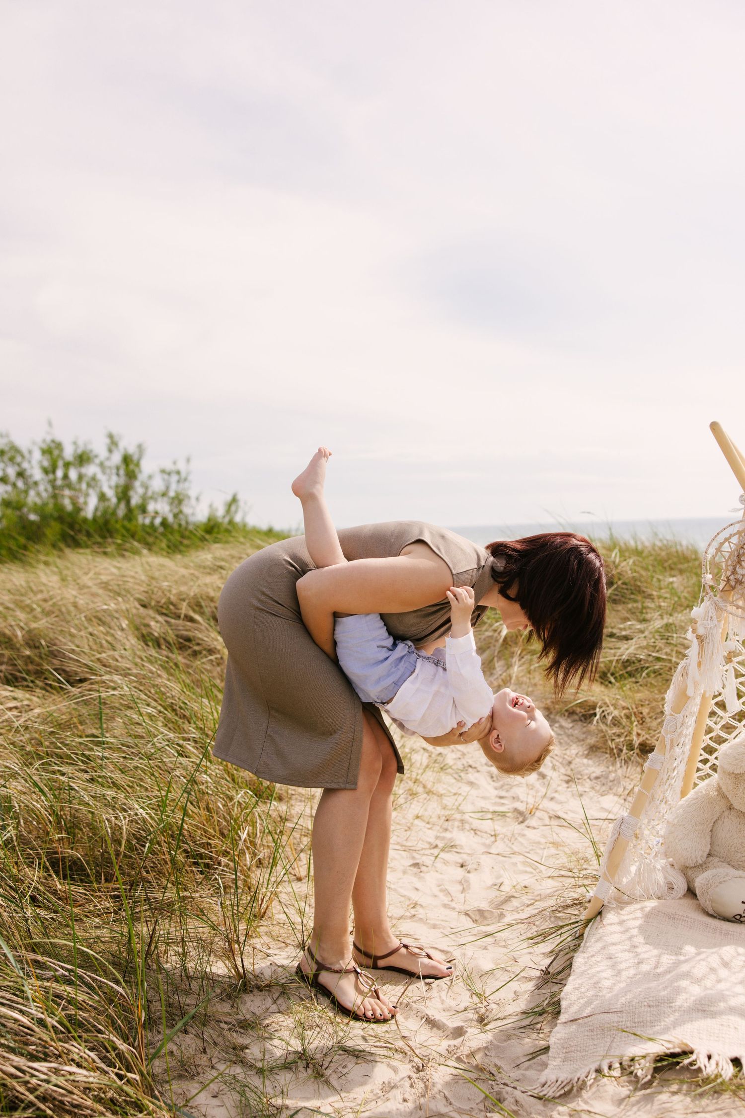 A heartwarming moment captured at a beach with tall grass as a child is playfully dipped backwards.