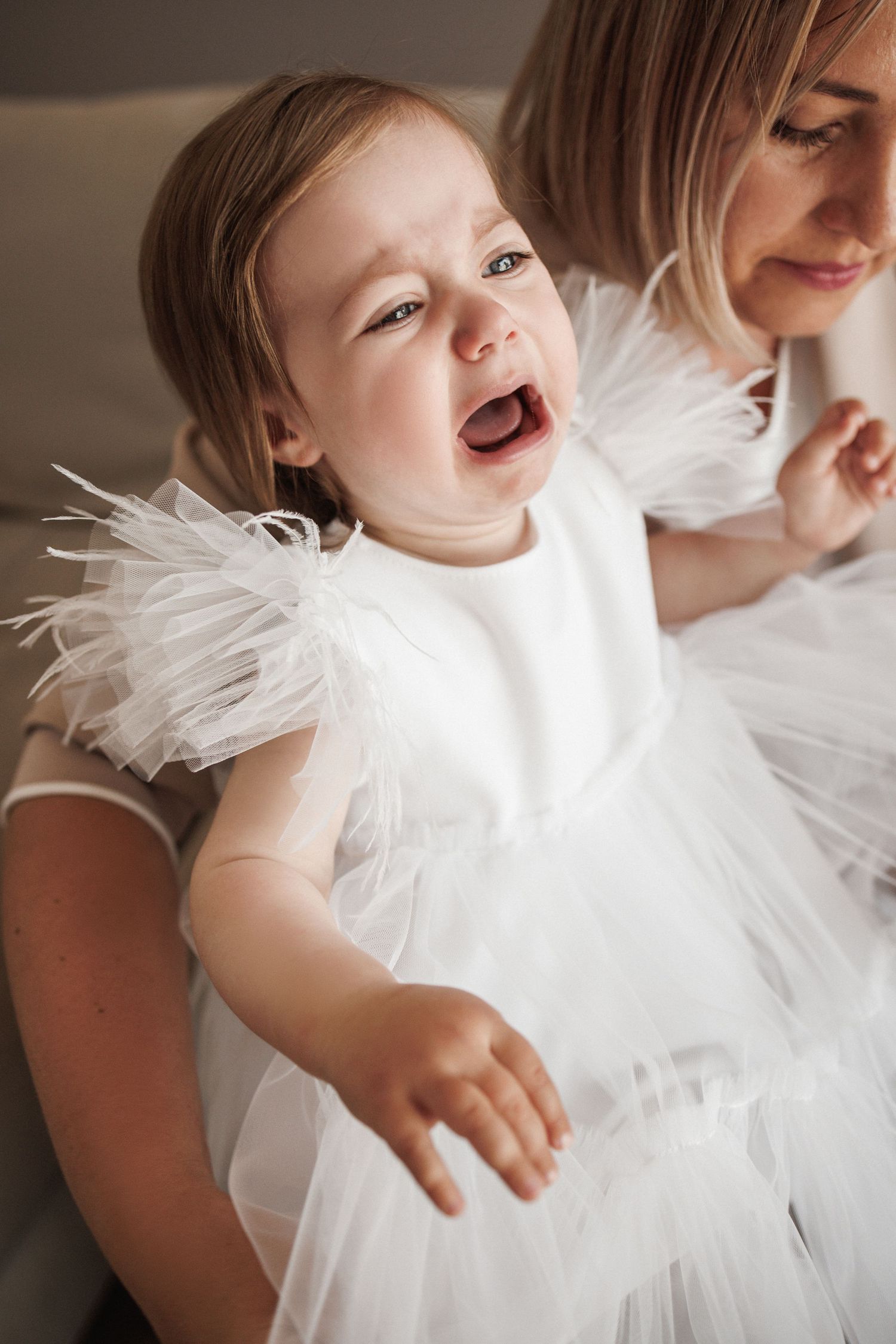 A baby in a white feathered dress laughs joyfully in a series of candid shots.
