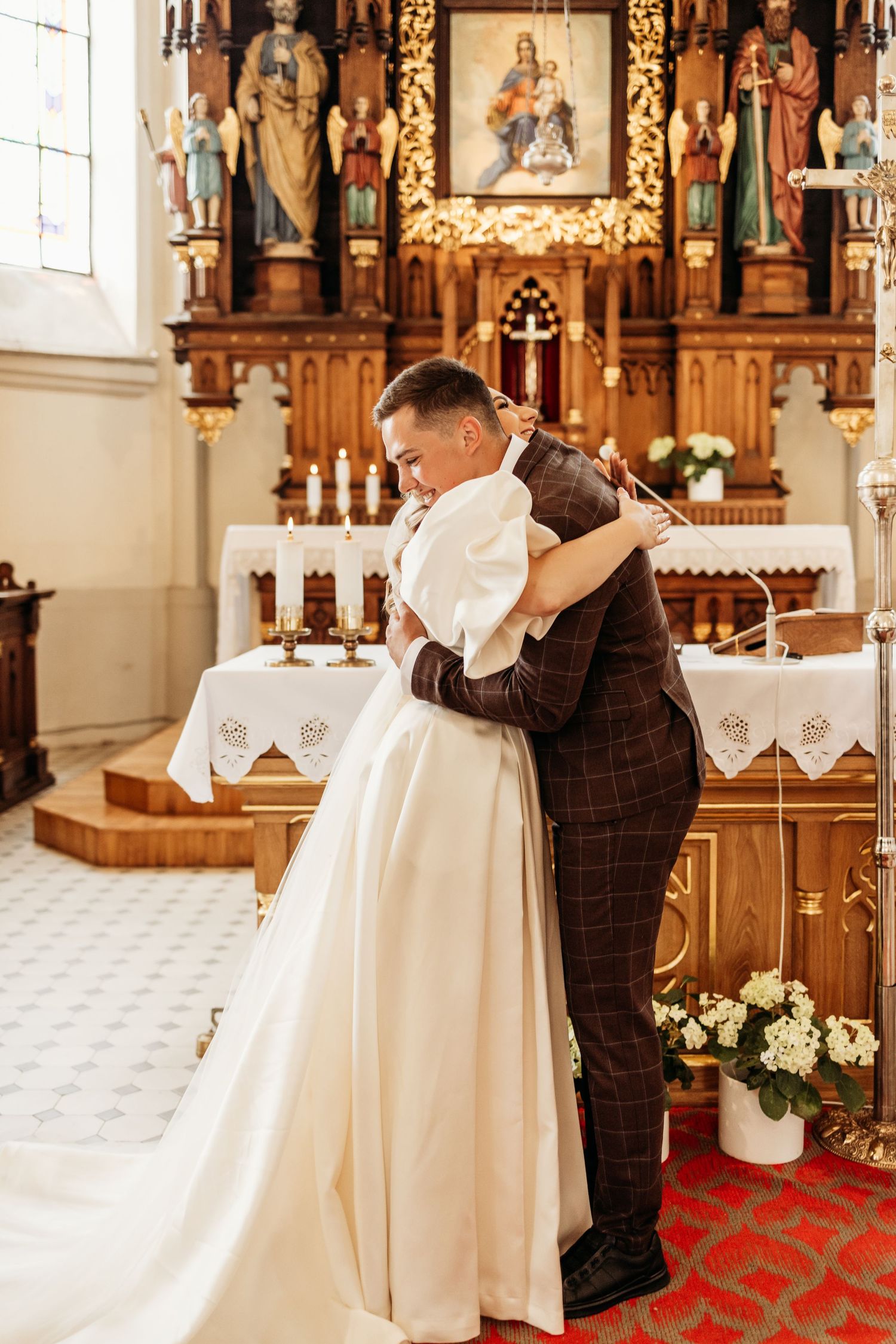 Wedding couple shares intimate moments in a traditional church with ornate wooden altars and religious statues.