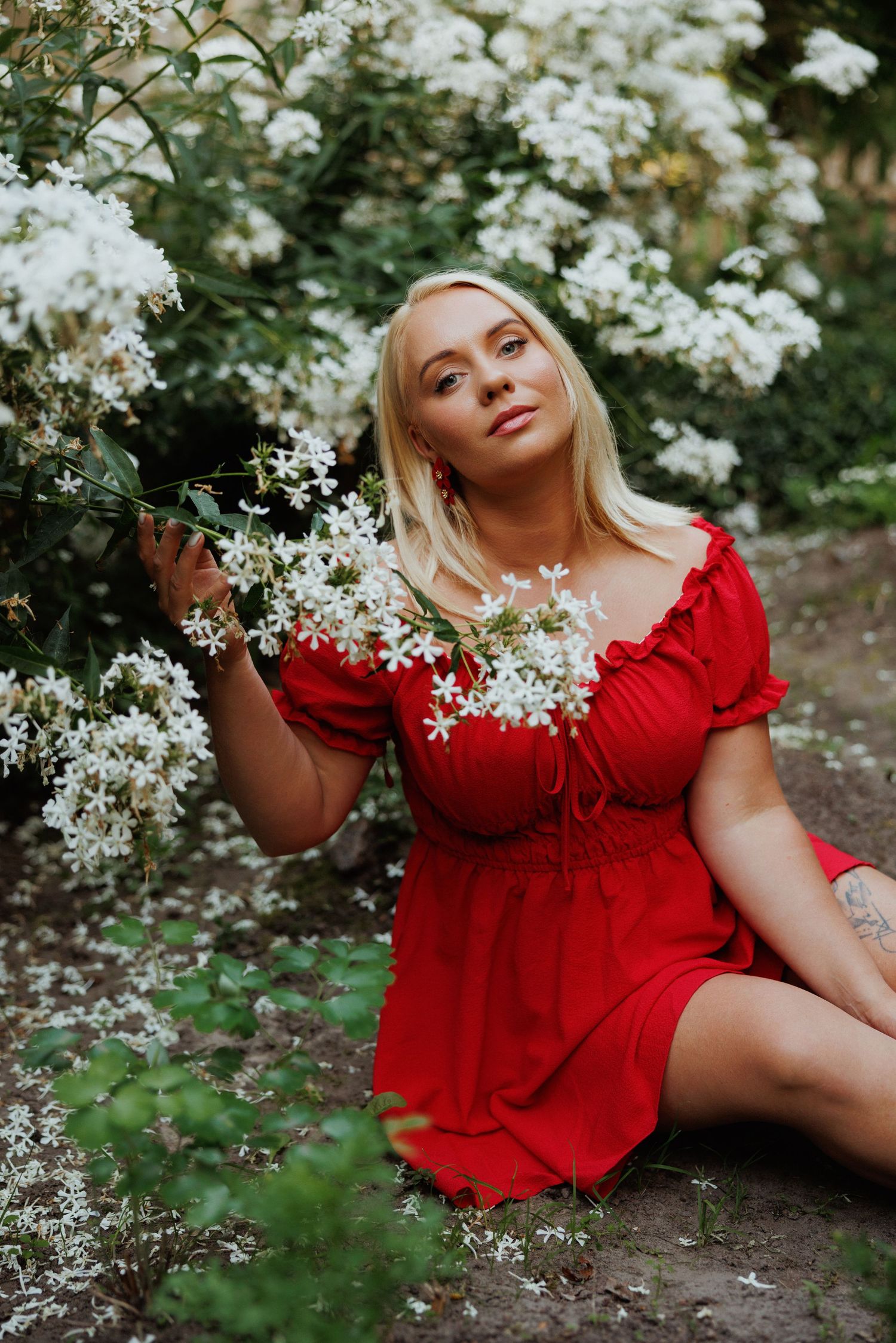 A person in a vibrant red dress poses gracefully among delicate white flowers in a garden setting.