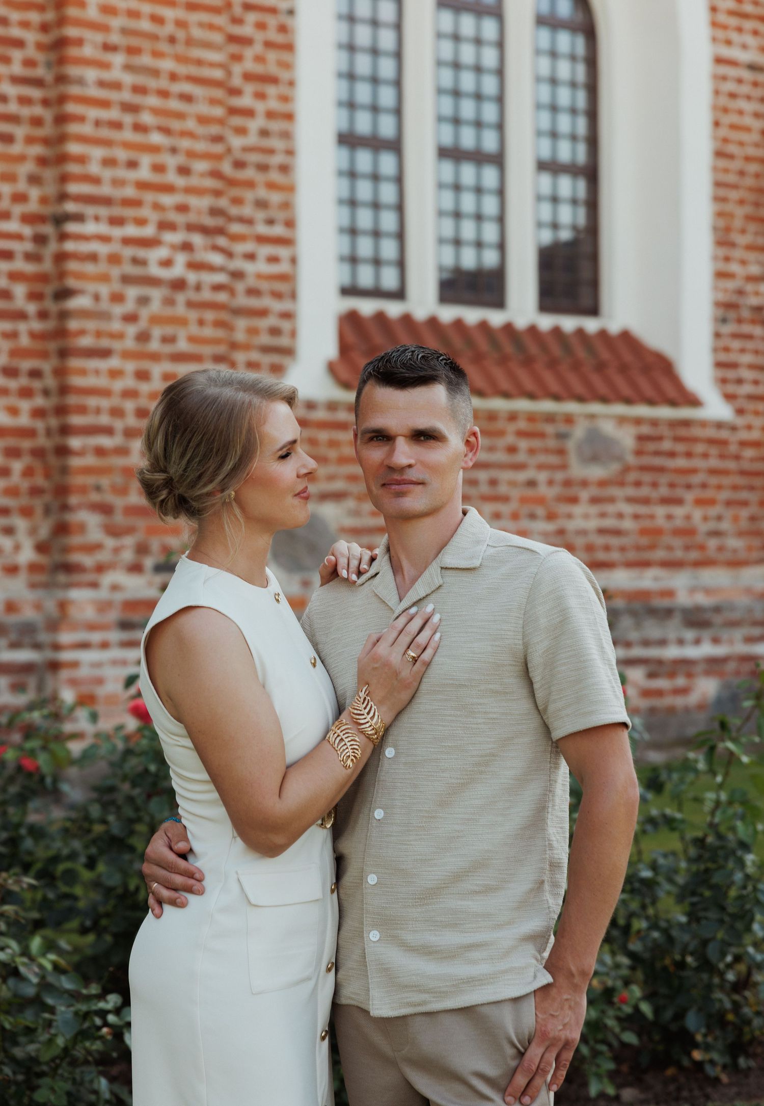 A couple in casual attire embracing outside a brick church building.