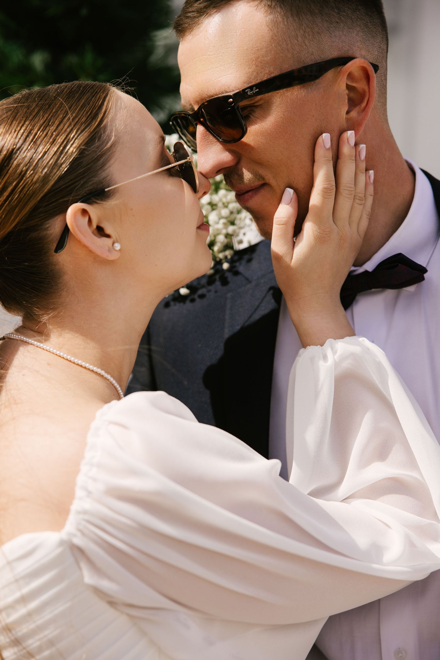 A tender moment between newlyweds wearing sunglasses in bright outdoor lighting.