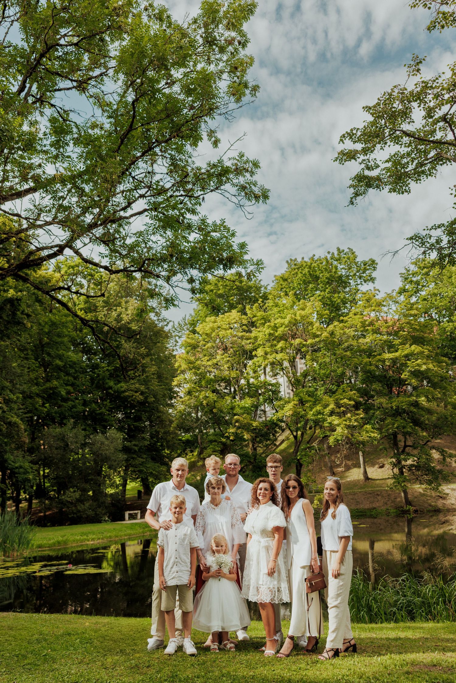 A group dressed in white outfits poses together on a grassy hillside during a sunny summer day.