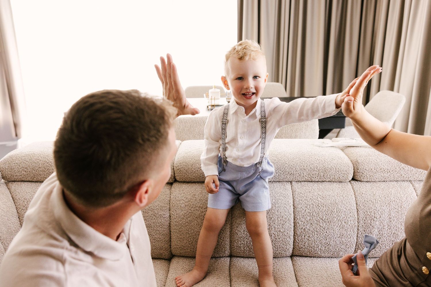 Family enjoys playful moment together on gray couch in living room during casual weekend at home.