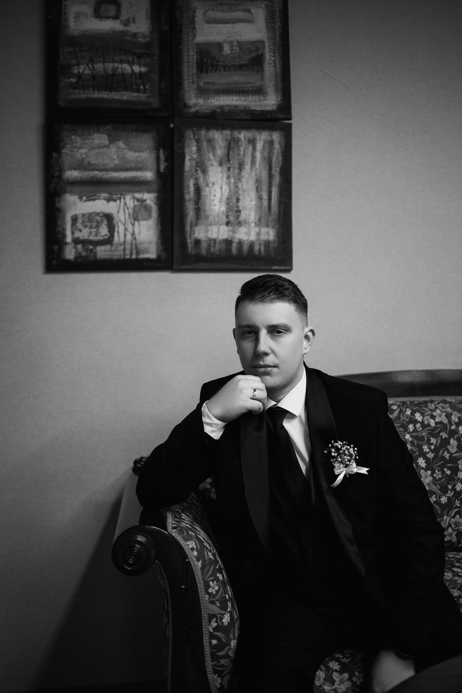 Dramatic black and white portrait in formal attire against vintage wall decor.