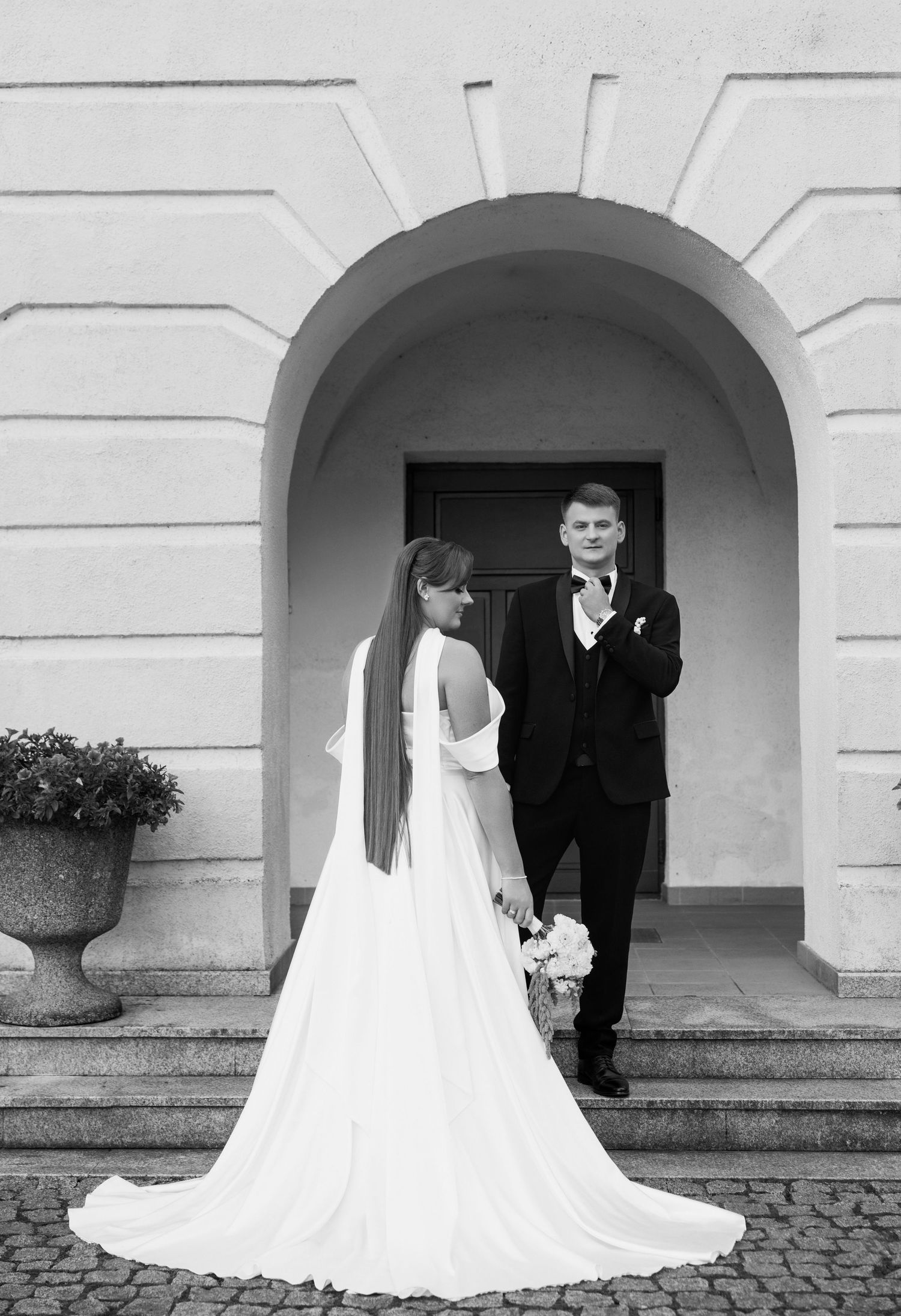 Black and white wedding photos showing a couple under elegant stone archways with a flowing white dress train.