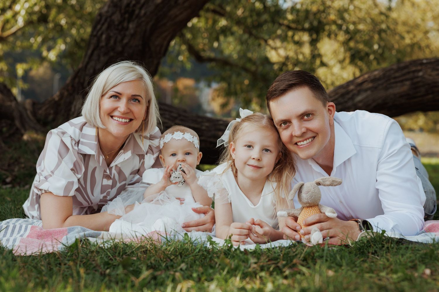 Family members dressed in white lying on grass during golden hour outdoor photo session.
