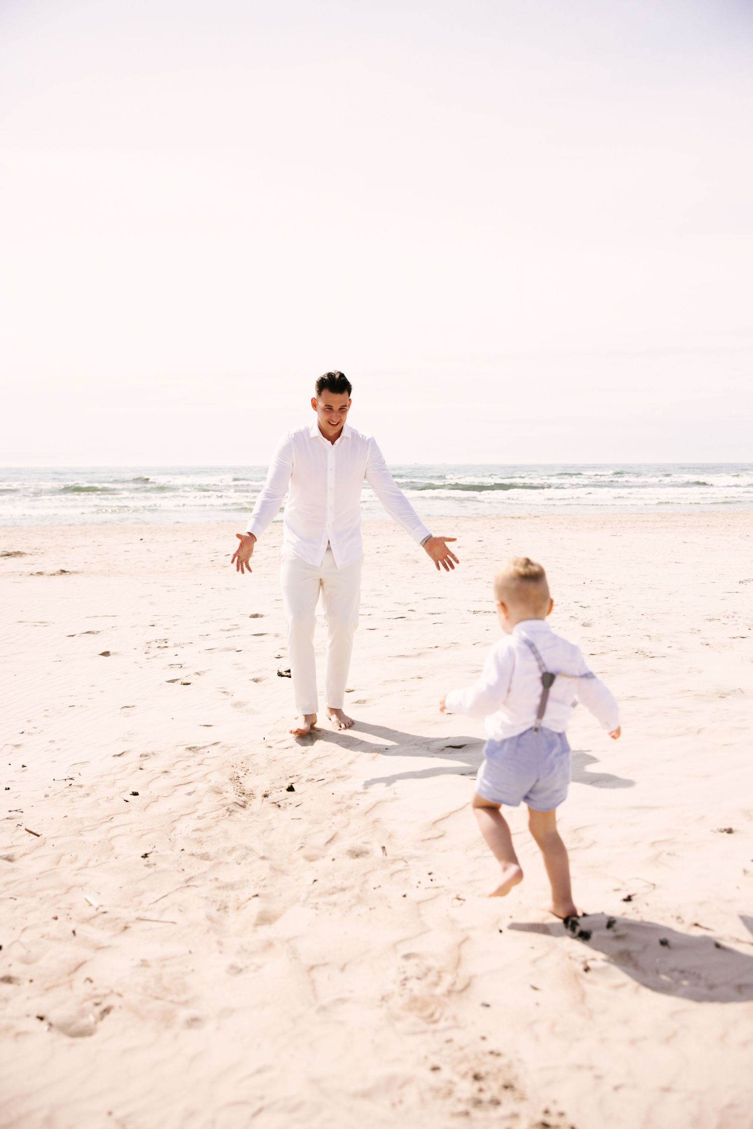 Playful beach scene with people in white clothing running on sandy shore.