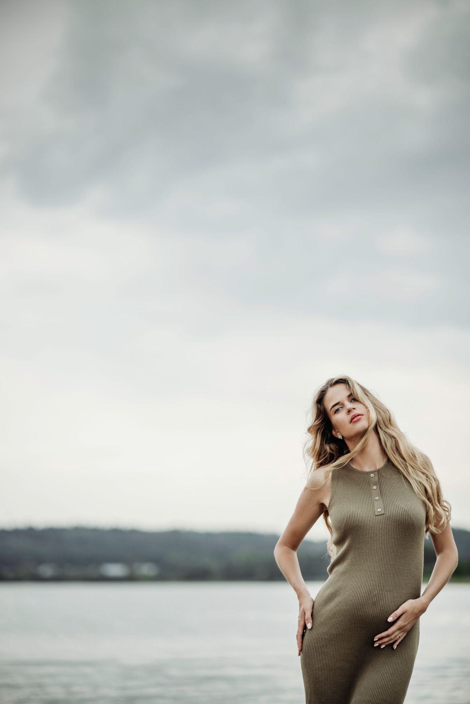 Maternity photoshoot in an olive dress against a serene waterfront backdrop.
