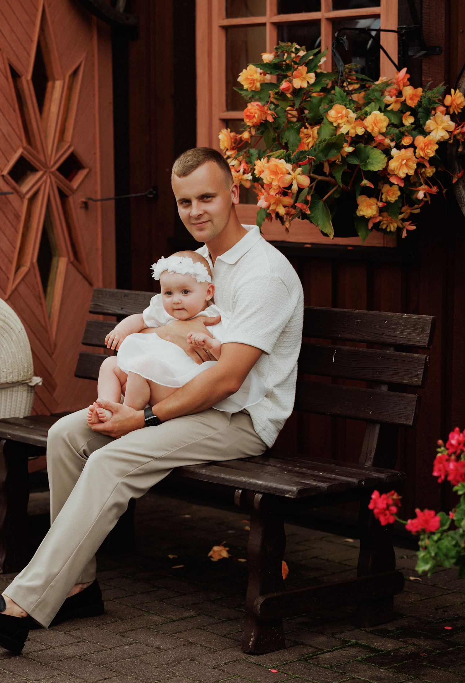 A family relaxes on a wooden bench surrounded by blooming orange and red flowers.