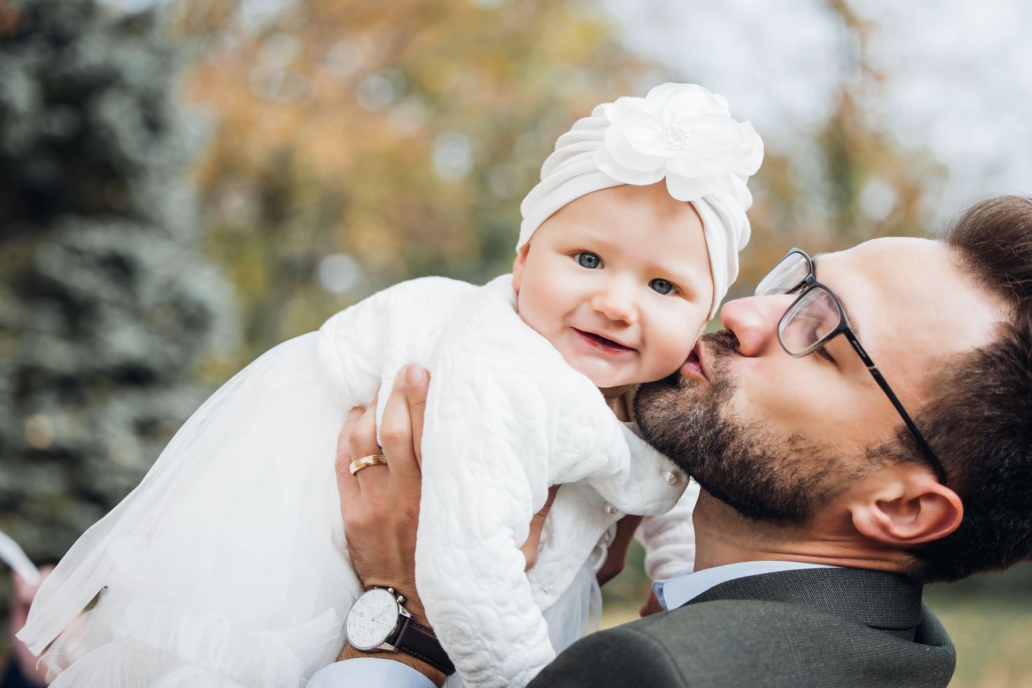 A tender moment between parent and baby in a white dress captured during an outdoor family photo session.