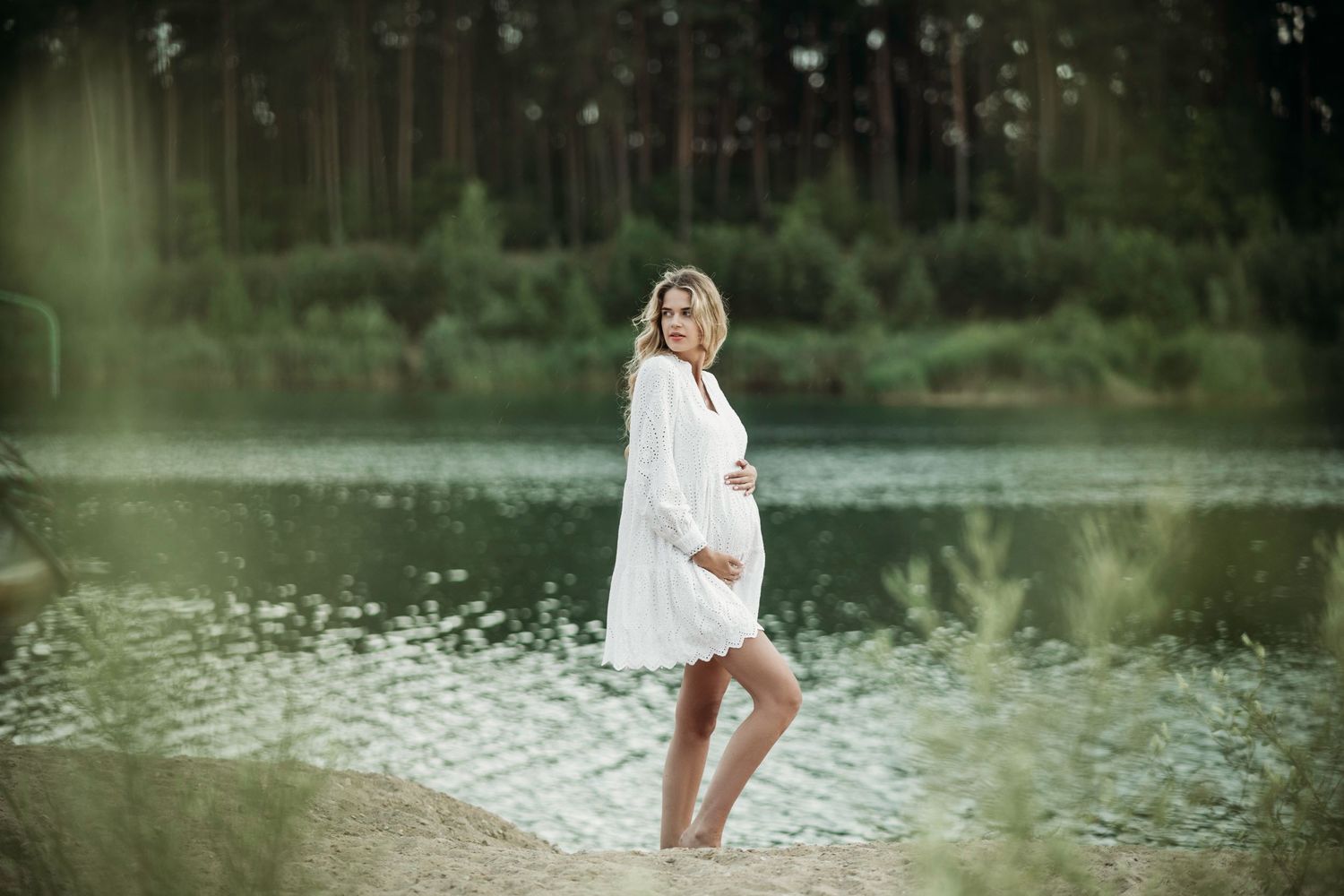 Ethereal maternity session captured by a lake with white flowing dress.