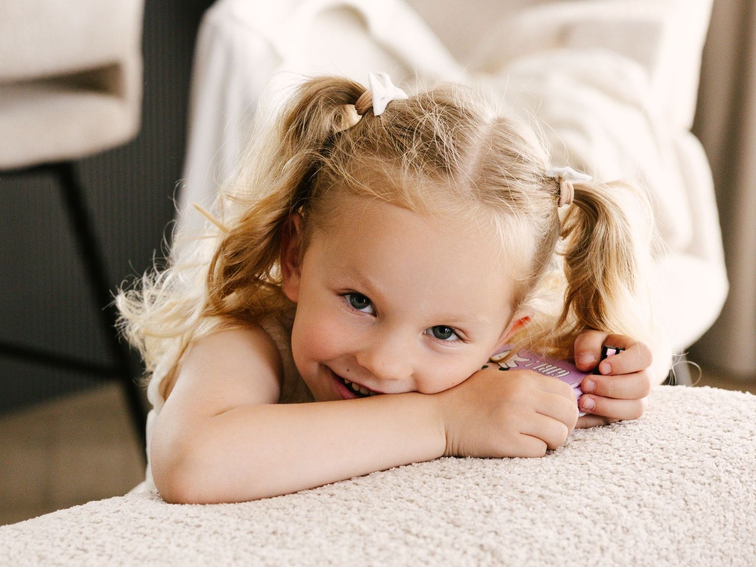 Young child with pigtails smiling while resting on white couch.