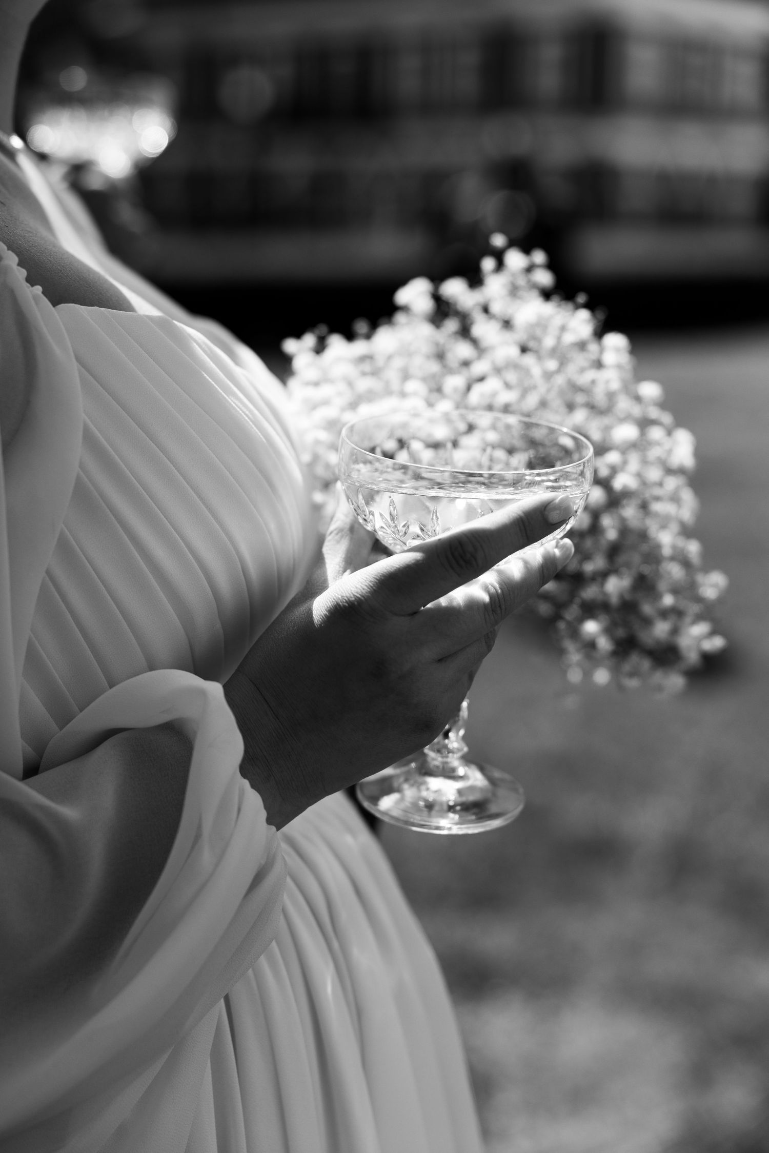A black and white photo of a bride holding a champagne glass with baby's breath flowers.