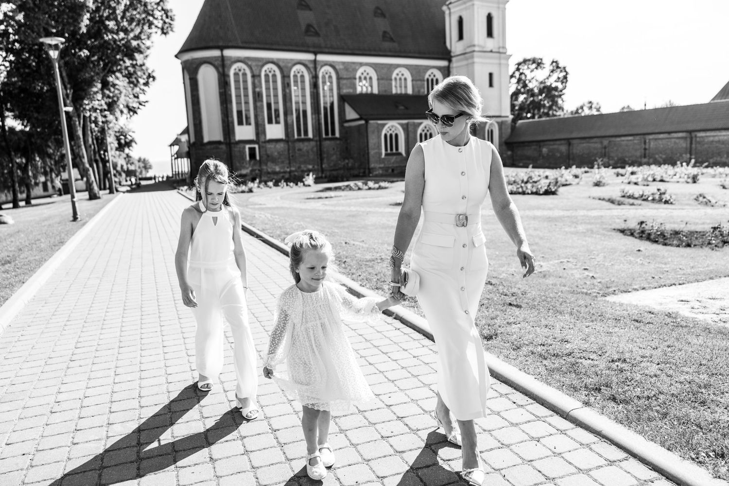 People in white outfits walking along a paved pathway outside a church on a sunny day.