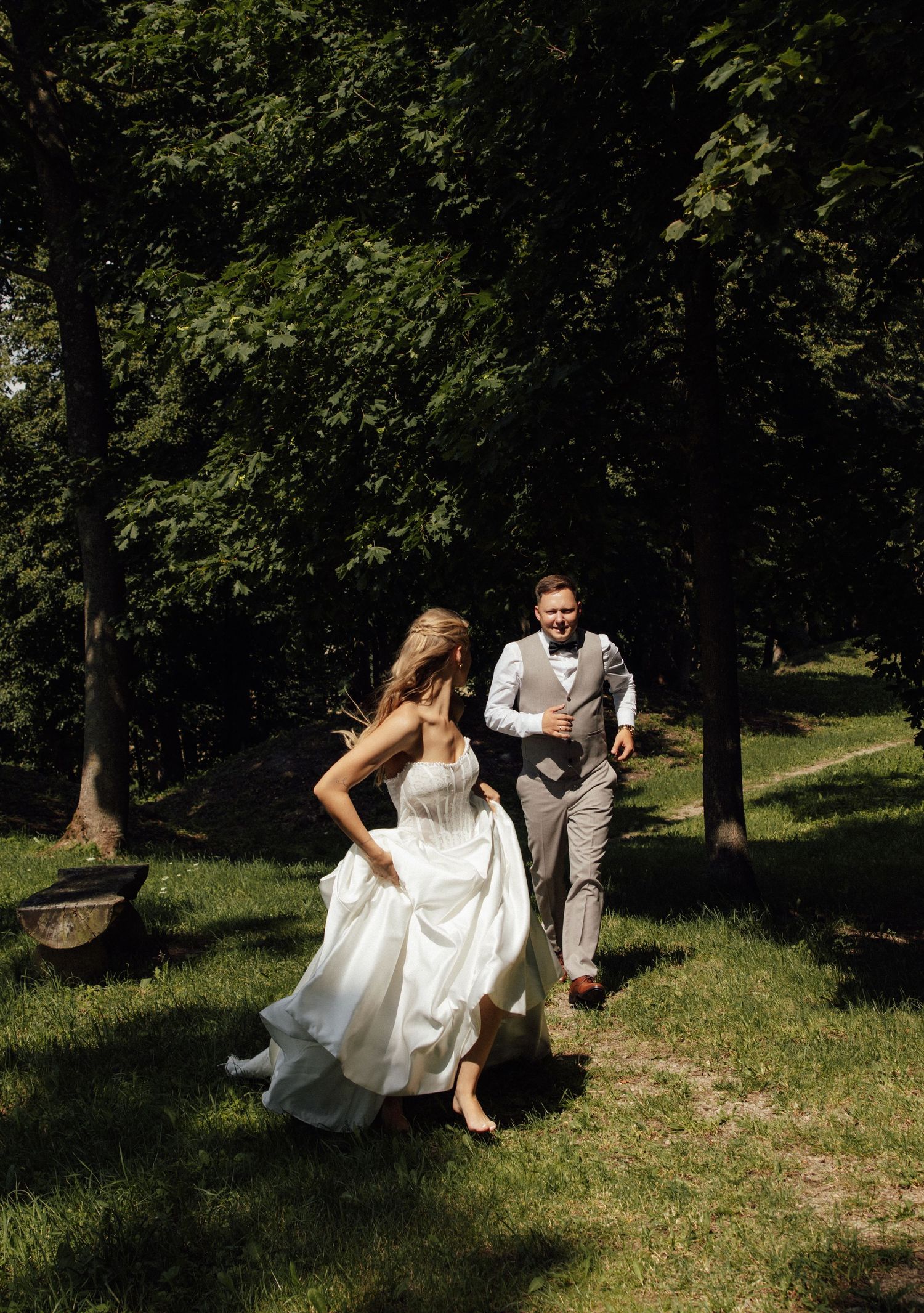 Bride and groom running joyfully through a lush green forest on their wedding day.