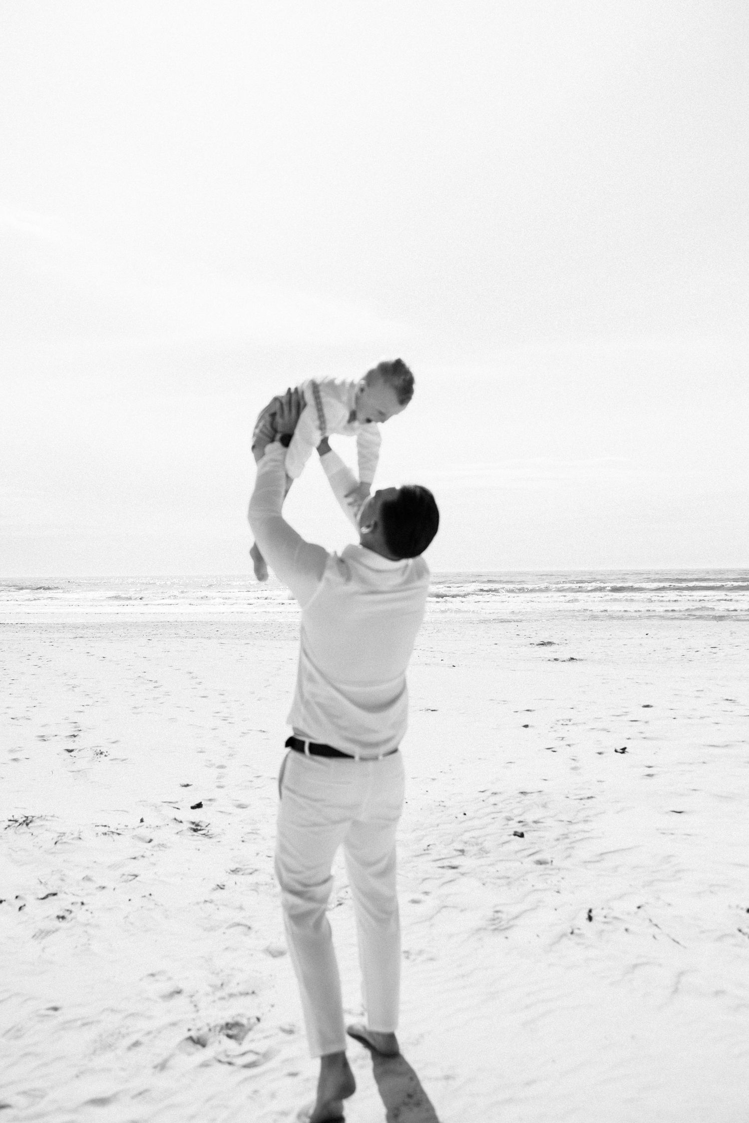 Black and white photos of playful moments on beach with family in matching outfits.