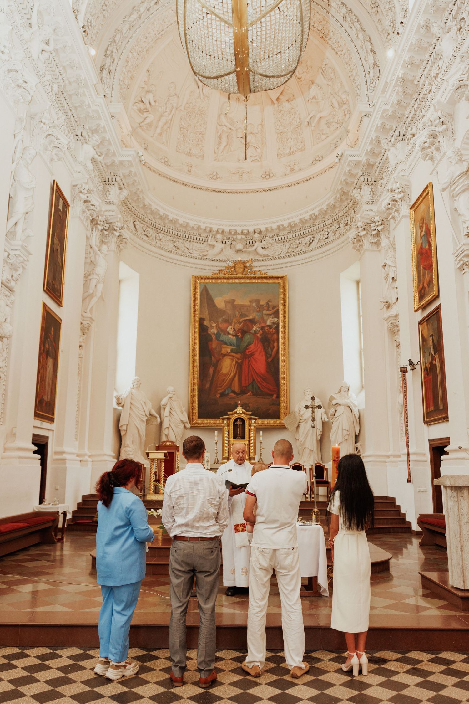 People admiring ornate religious artwork and architecture in a historic white baroque church interior with gilded details.