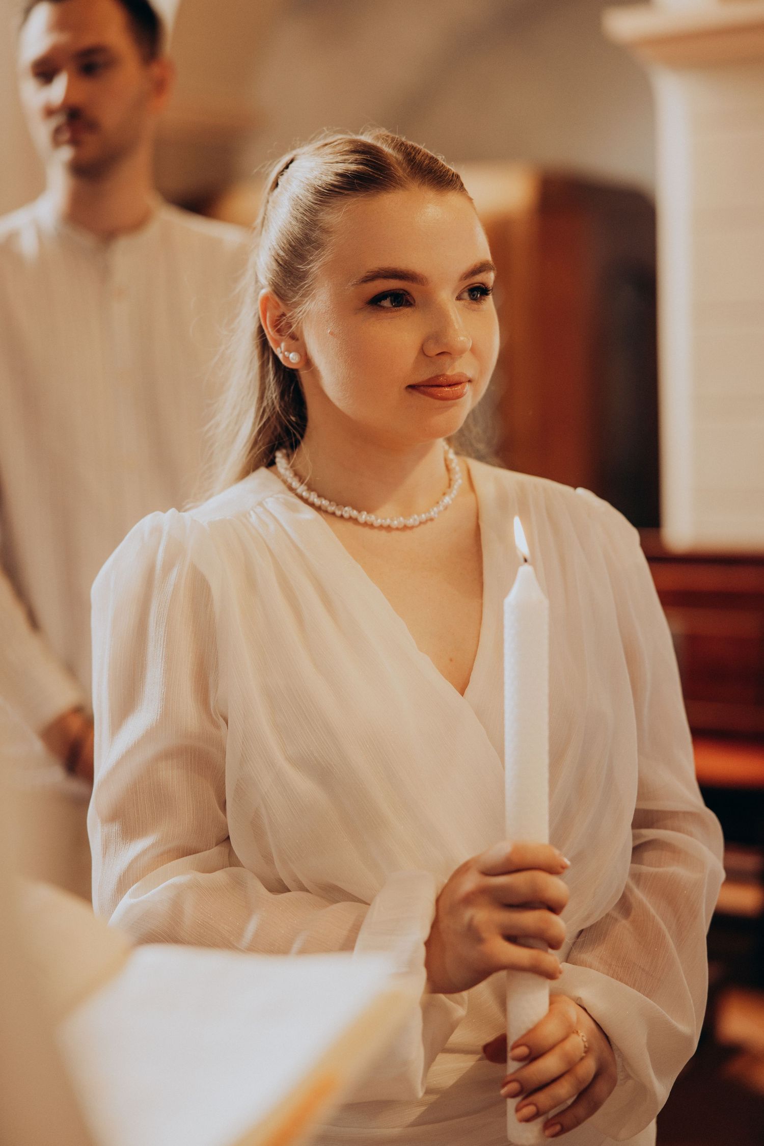 A person in white holding a candle during a formal ceremony or celebration.