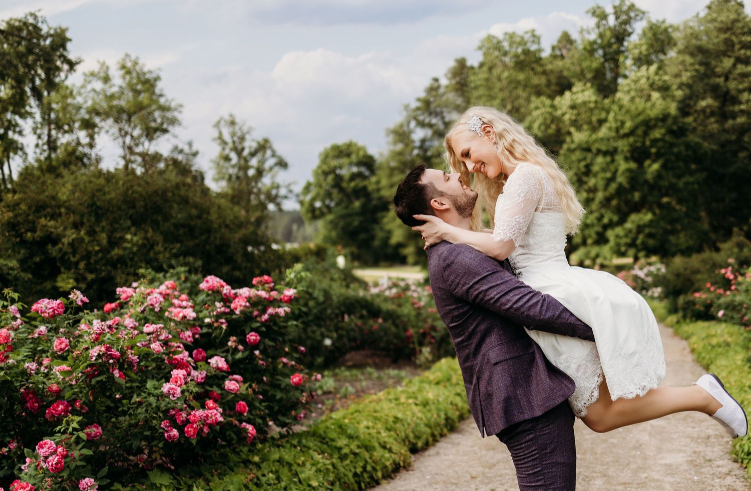 A romantic outdoor wedding celebration with a couple dancing in a garden path surrounded by blooming pink roses.