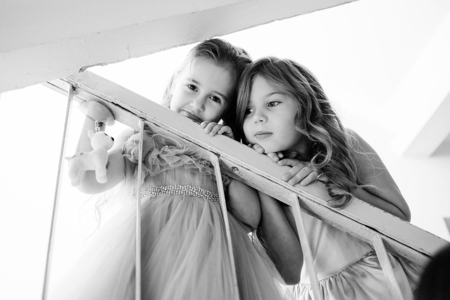 Two children peek through white sheets hanging indoors in this black and white photograph.