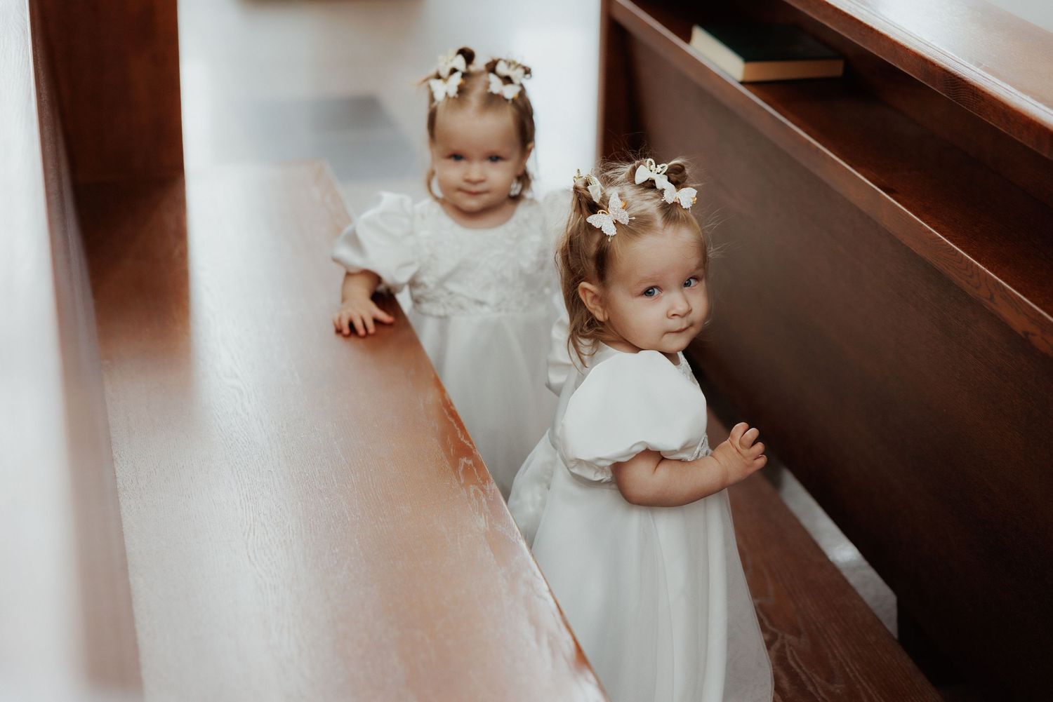 Children in white dresses descend wooden stairs during what appears to be a formal event or celebration.