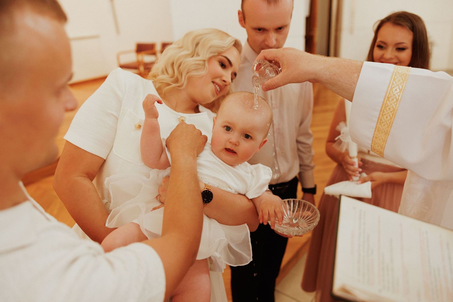 A baptism ceremony takes place in a church as attendees in white gather around.
