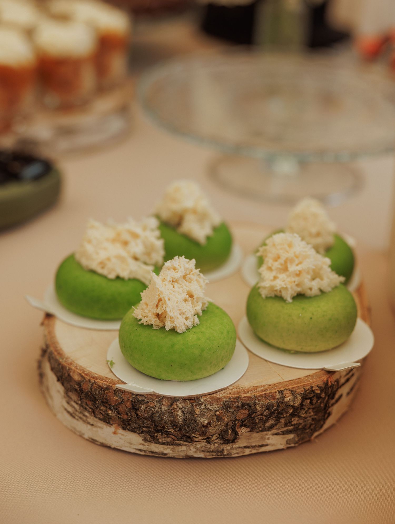 Green macarons topped with cream filling displayed on a rustic birch wood slice.
