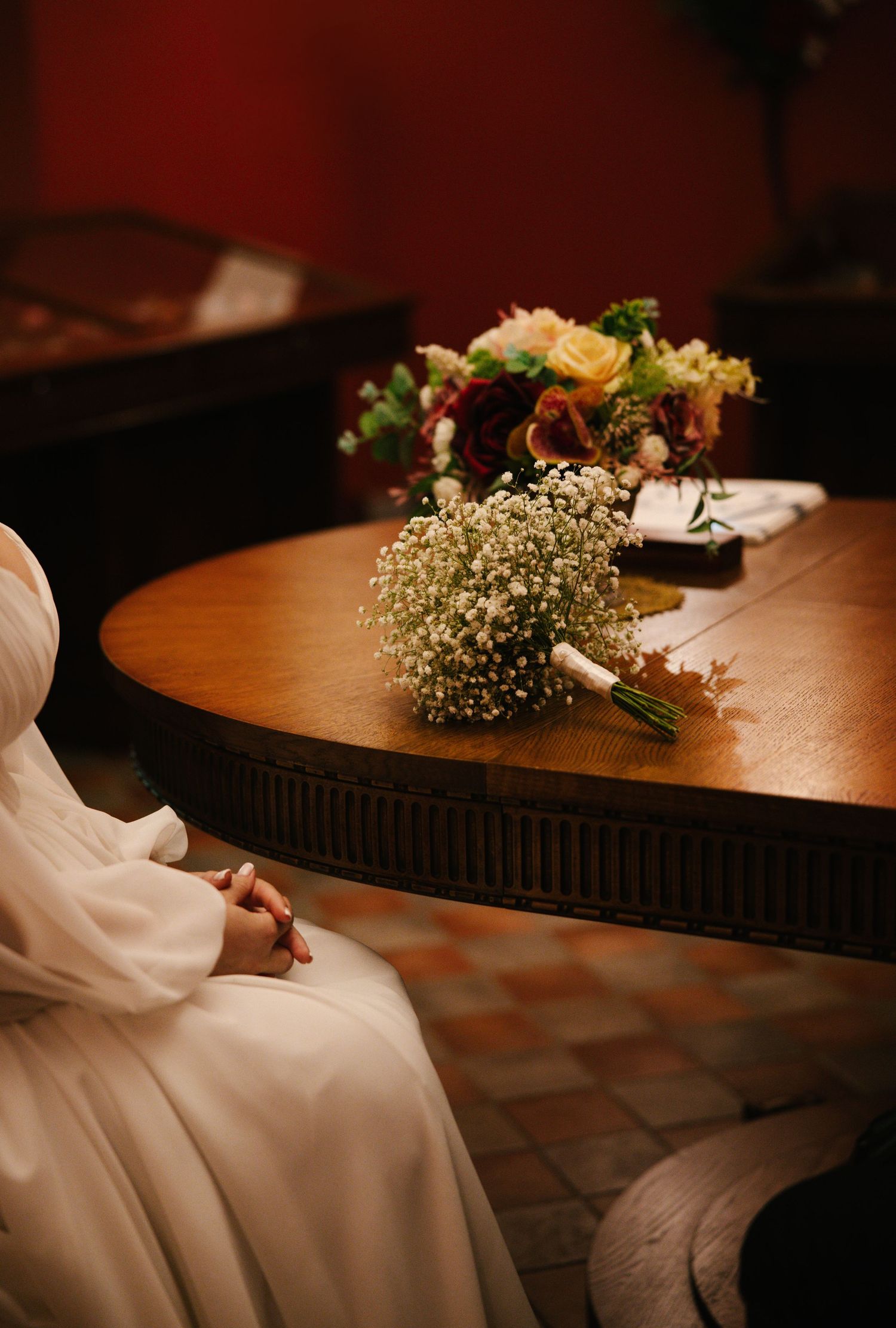 A wedding bouquet with baby's breath and roses rests on a wooden table beside flowing white fabric.