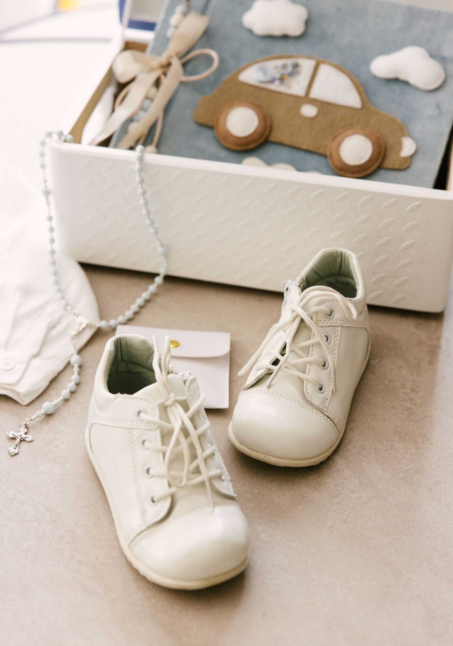 White baby shoes and toy car on light blue background with cloud decorations.