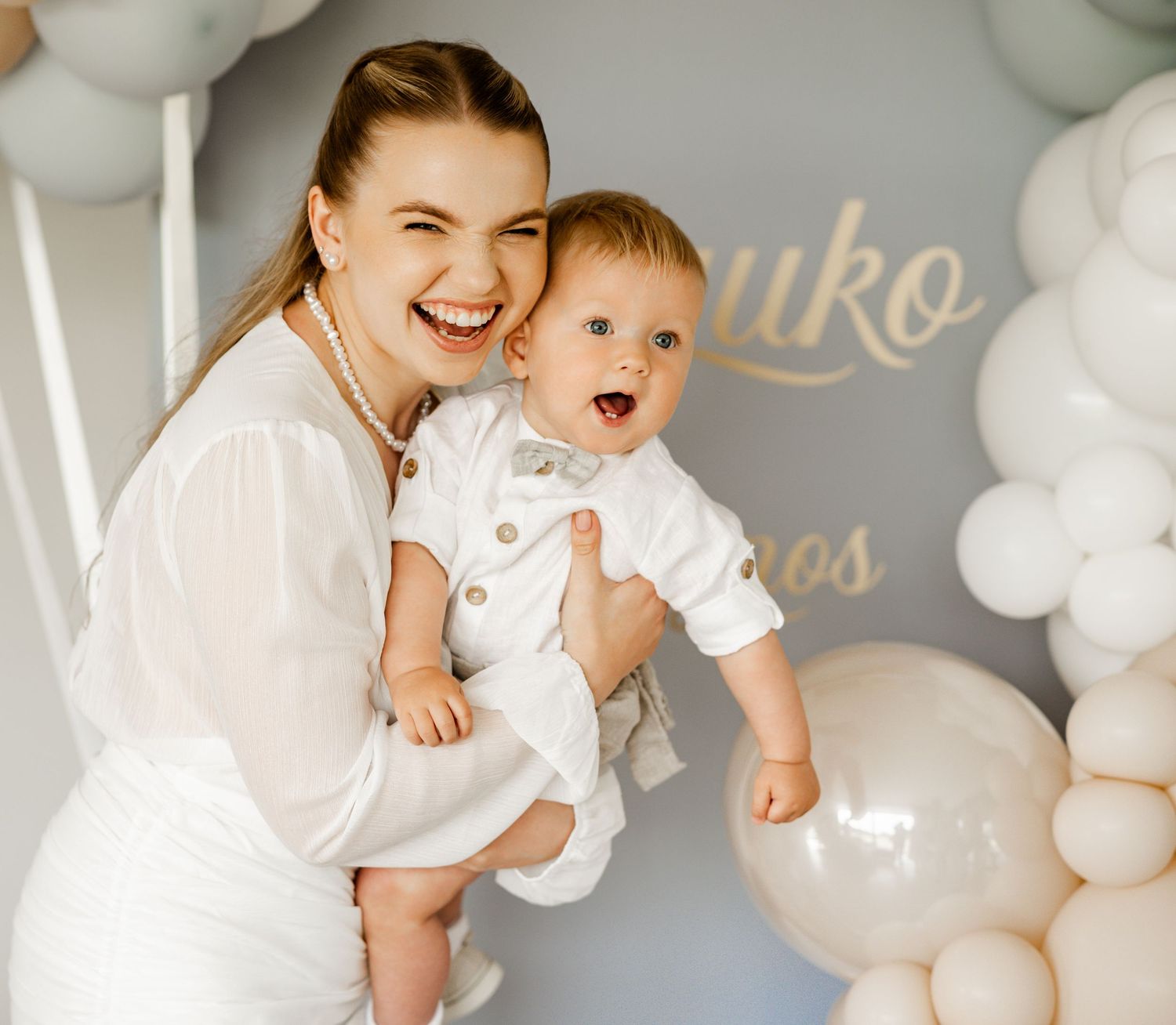 Celebratory scene with white and pastel balloon decorations against a grey wall.