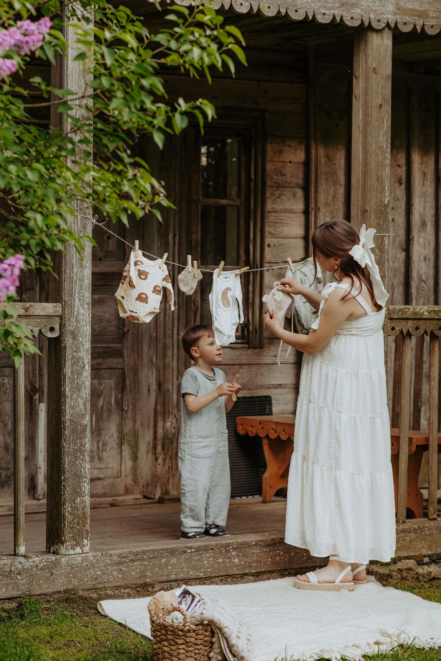 White baby clothes hanging on clothesline against rustic wooden cabin backdrop.