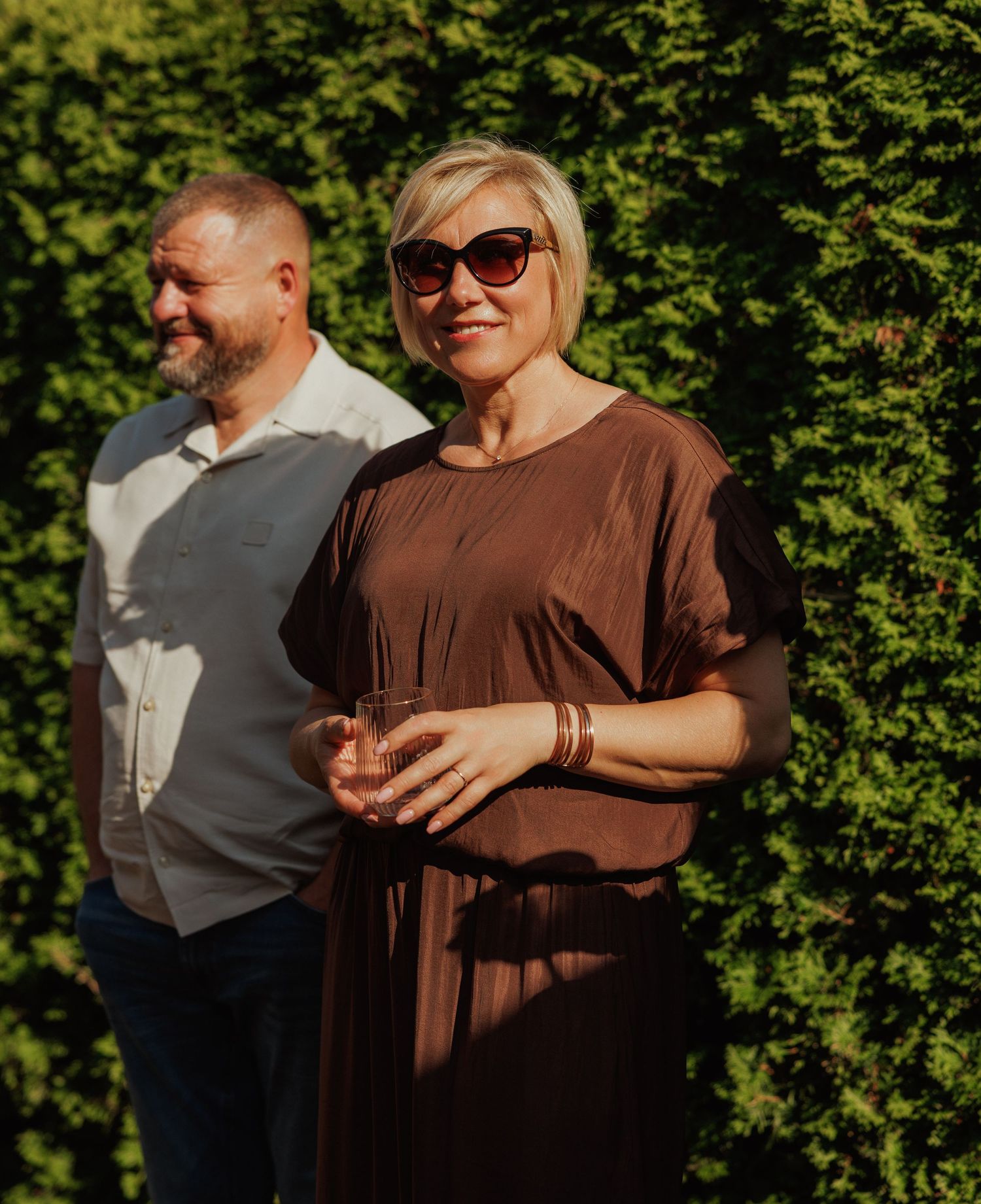 People gathered outdoors on a sunny day with green foliage in the background.