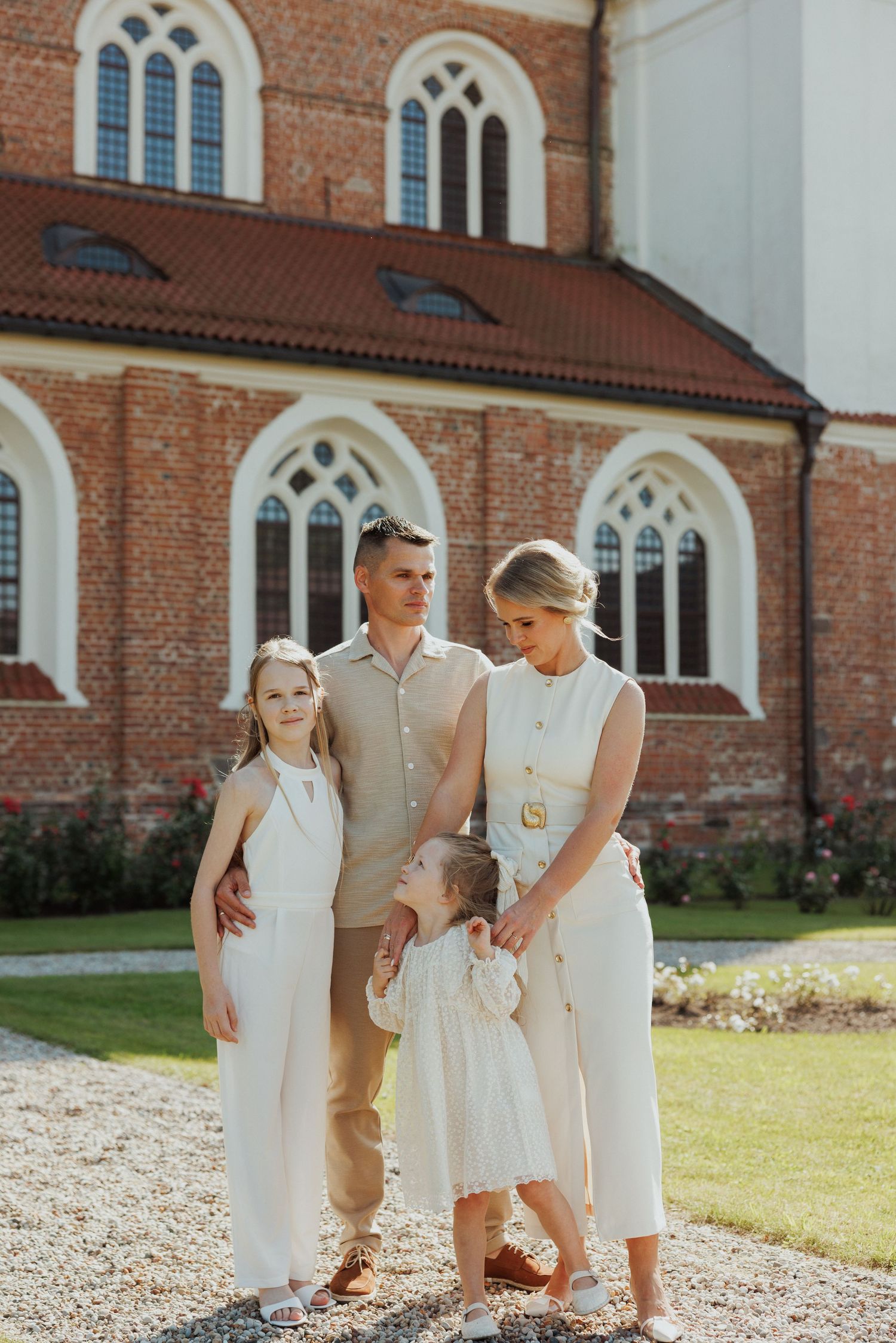 Family group in coordinated white and beige outfits posing outside a historic brick church.