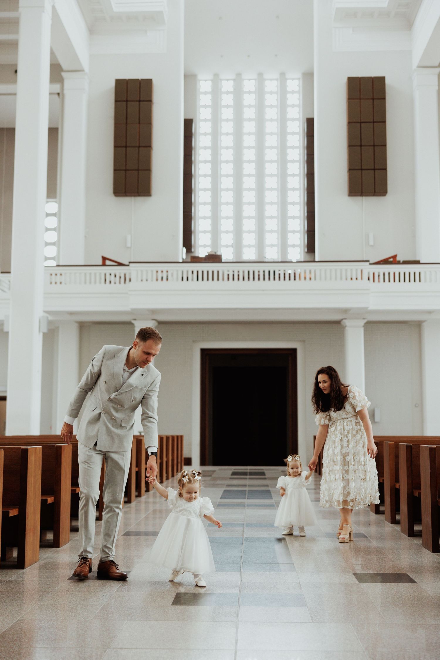A series of sweet moments between adults and a small child in white dresses within an elegant white church interior.