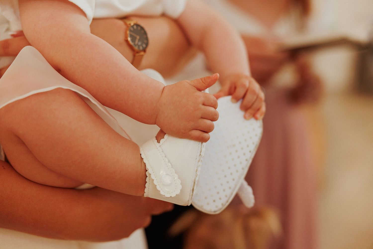 Close-up shots of delicate white baby shoes being held against a warm background.