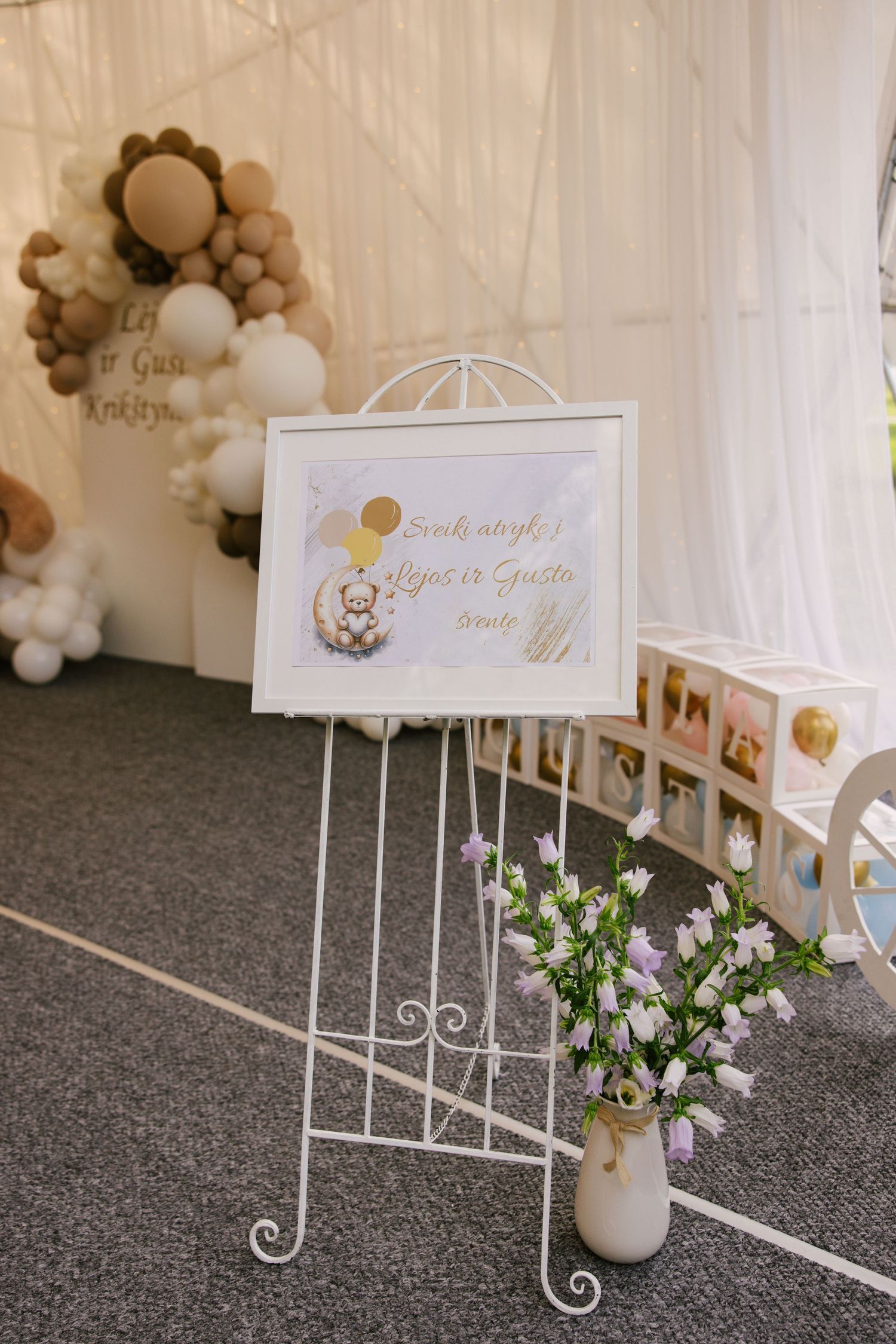 White decorative easel stand with welcome sign and balloon arch in neutral tones.