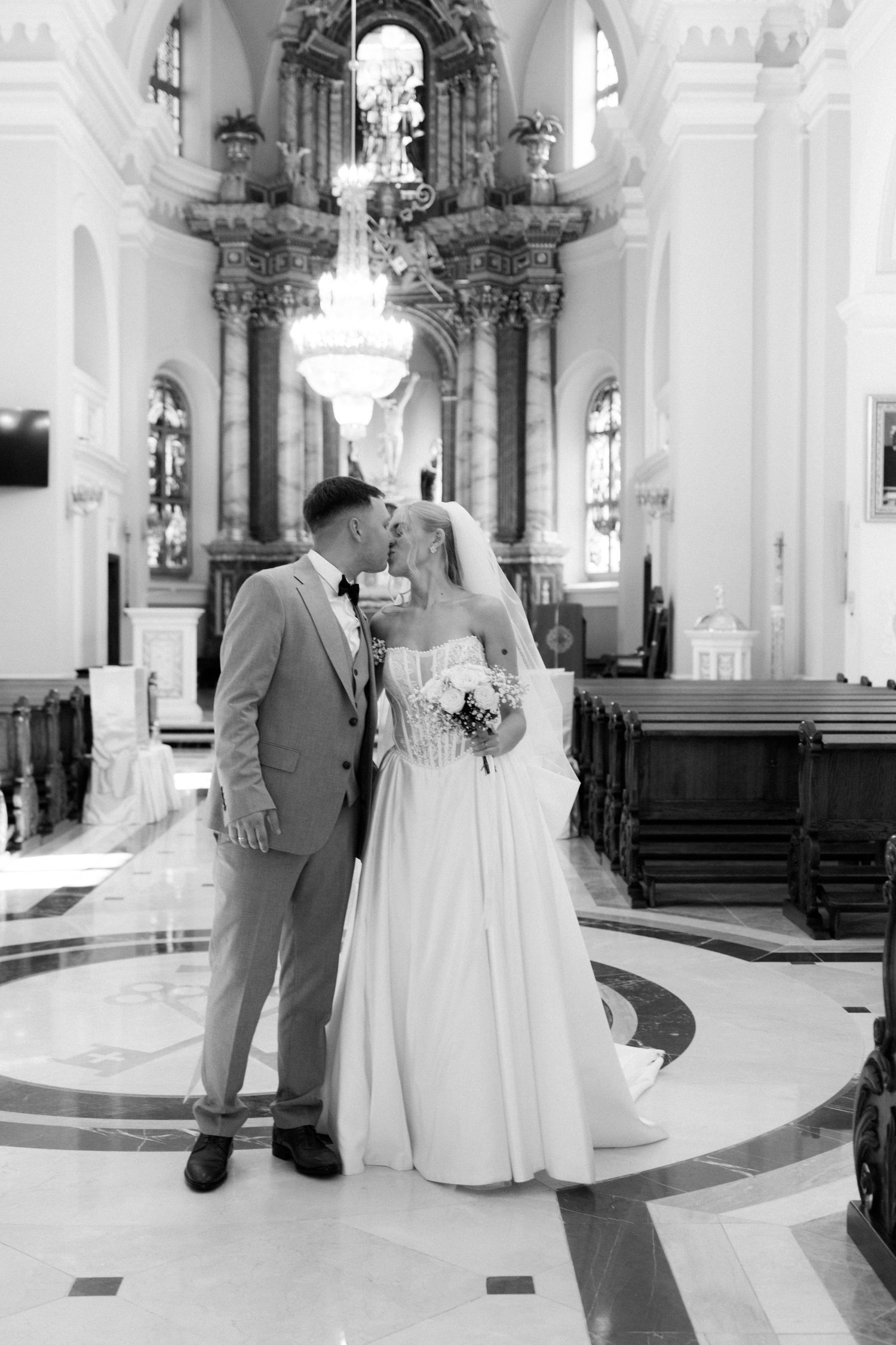 Black and white photo of a bride and groom sharing a kiss at the altar inside an elegant church.