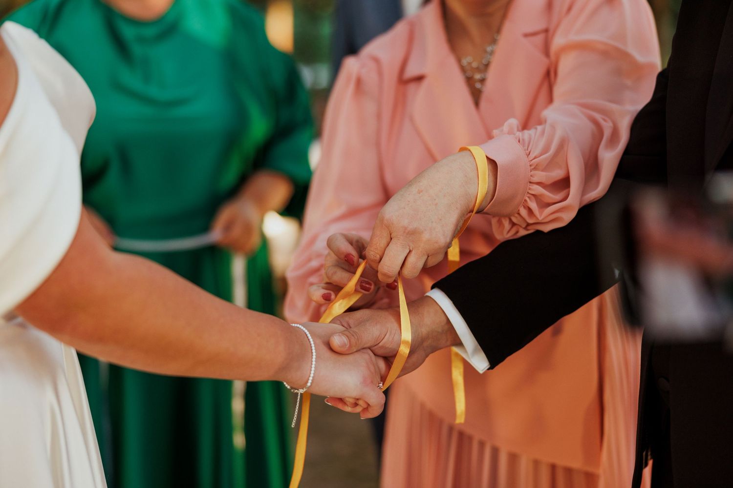 Wedding guests in green and pink attire participate in unity candle lighting ceremony.