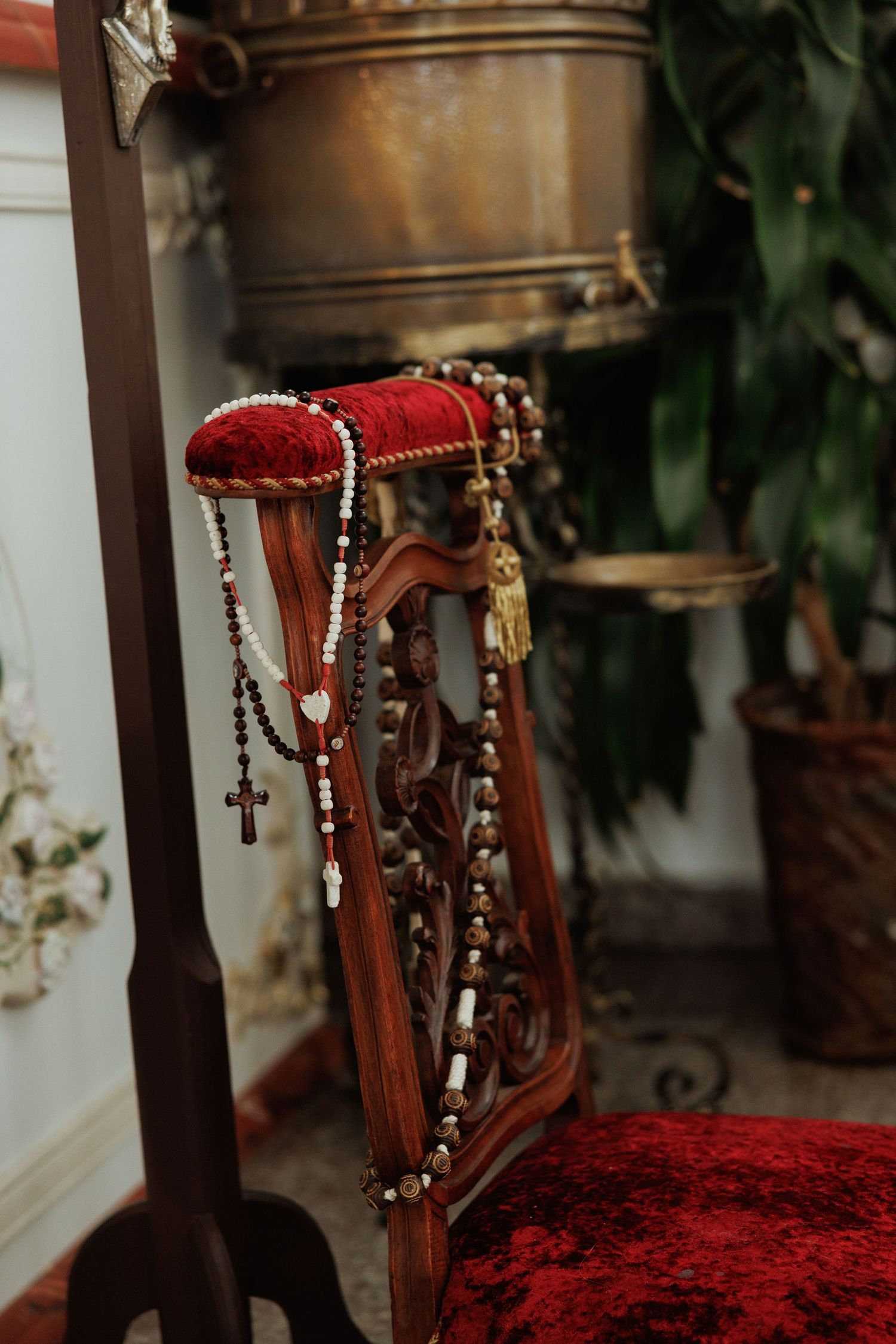Ornate red velvet chair with carved wooden details and decorative rosary beads in an elegant interior setting.
