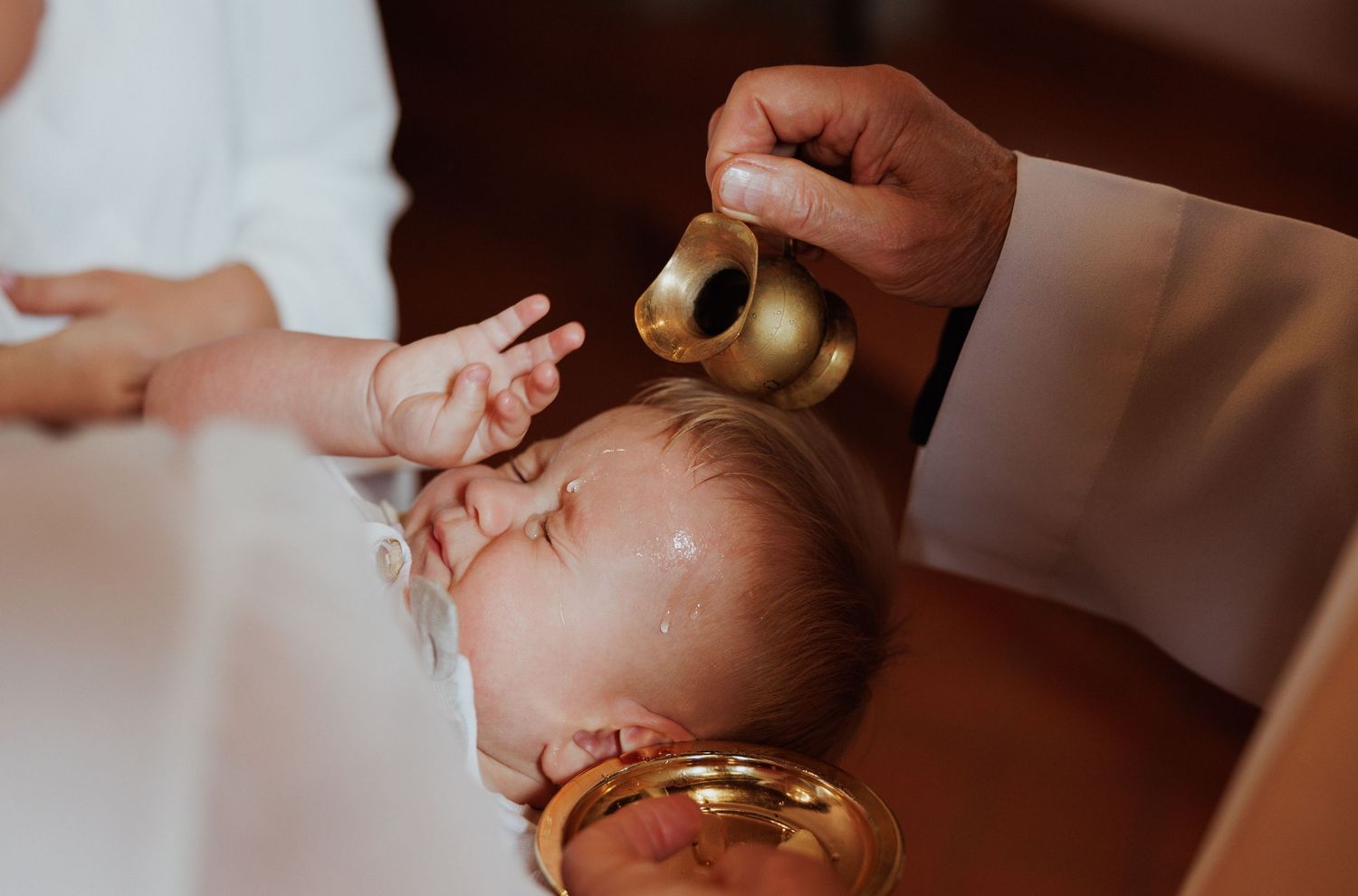 A baby receiving a traditional blessing ceremony with golden bells held by gentle hands.