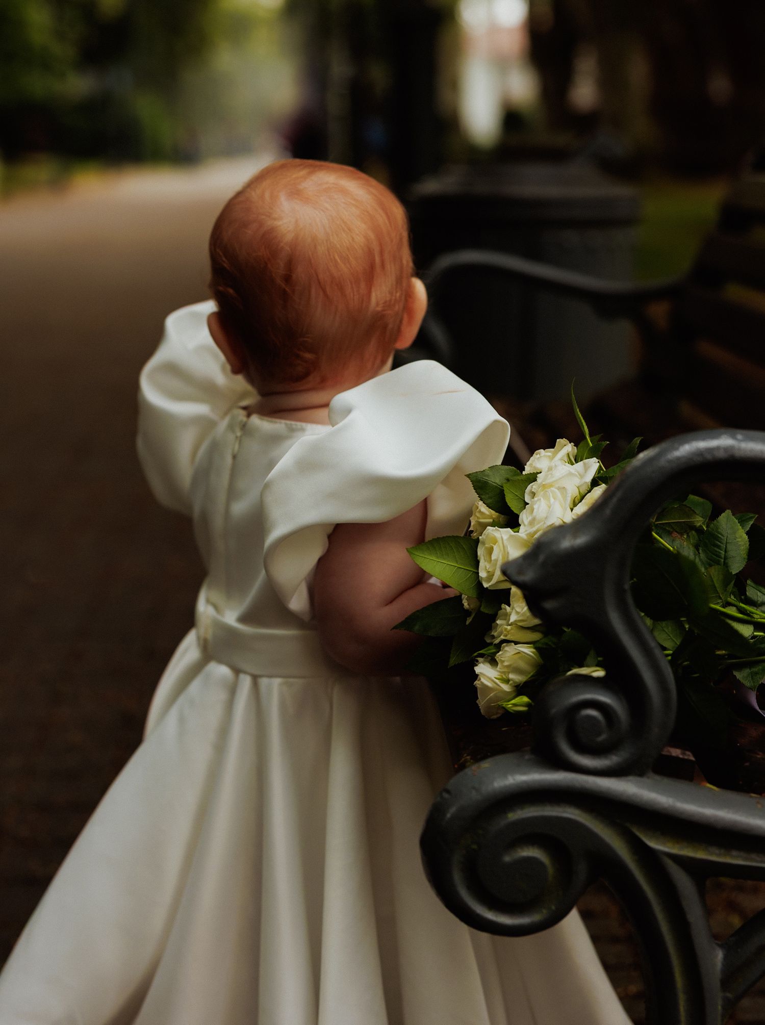 Close-up of white baptismal gown detail with wrought iron and flowers in background.
